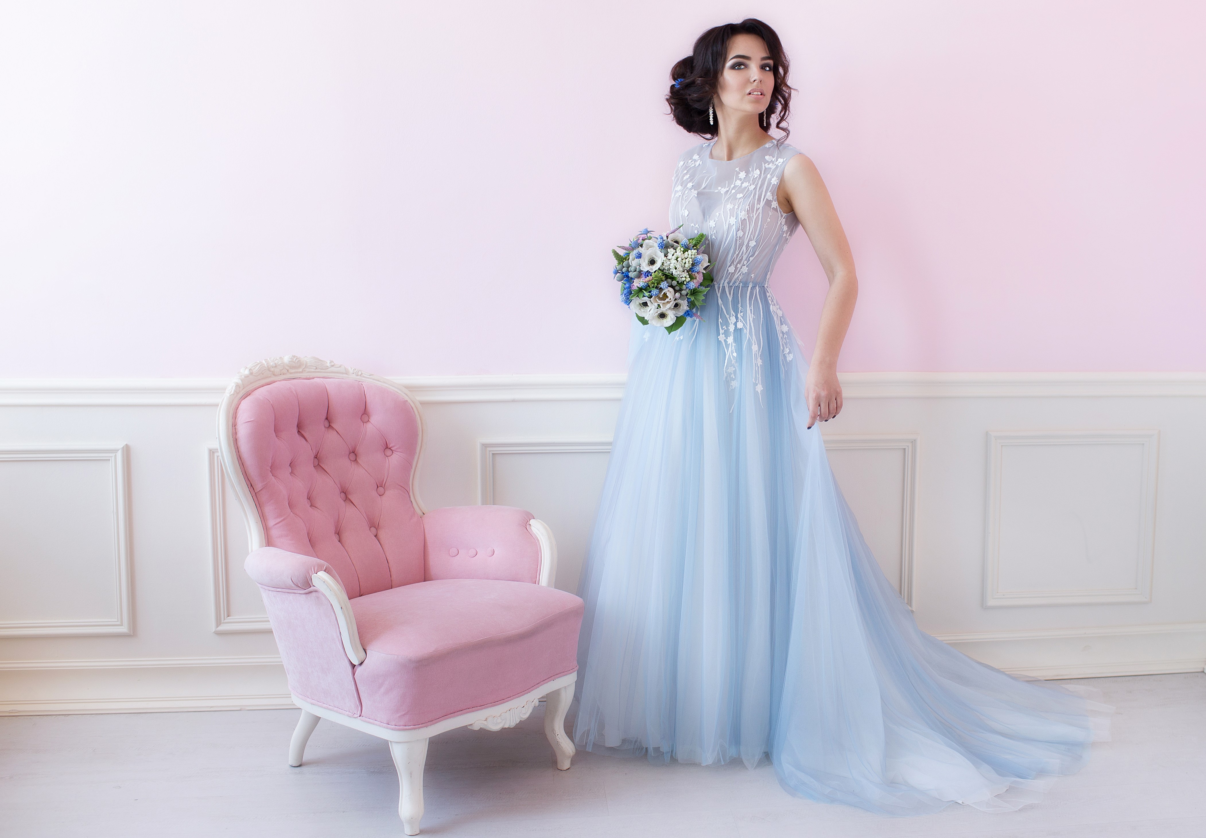 Woman in blue dress holding bouquet near pink armchair HD Wallpaper