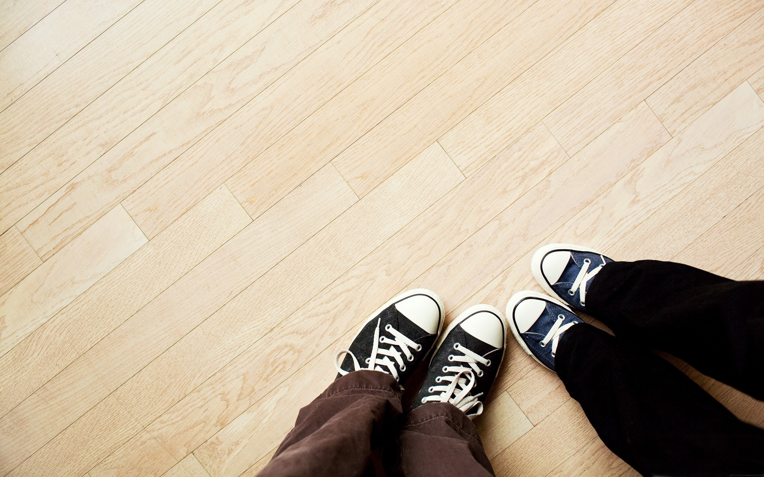Two pairs of feet wearing sneakers on a wooden floor HD Wallpaper