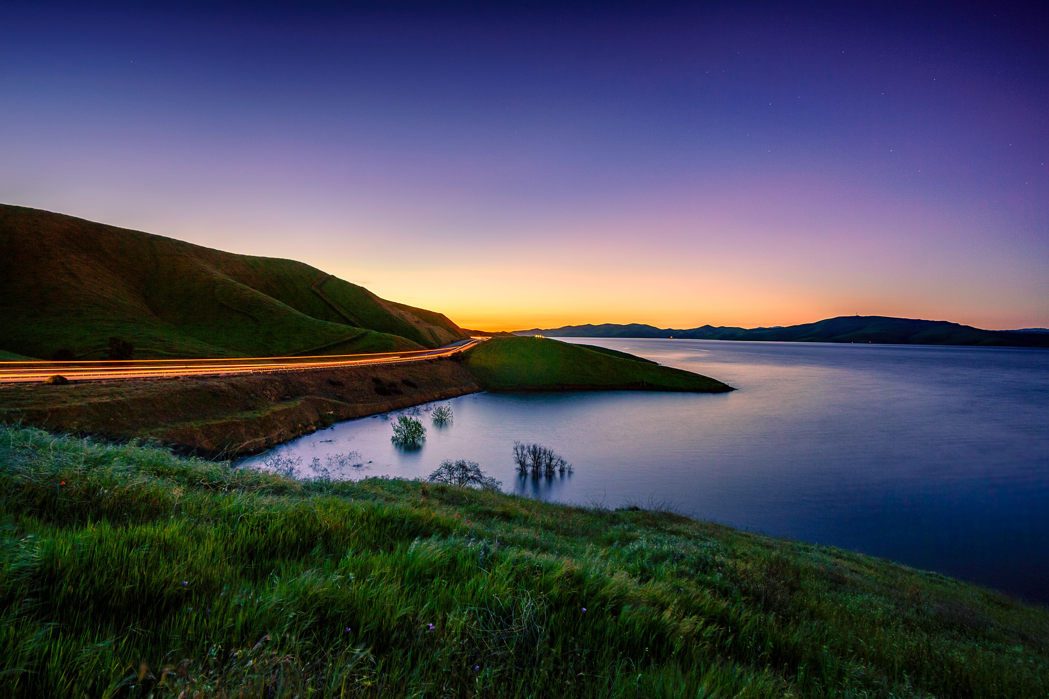 San Luis Reservoir at sunset with road and grass HD Wallpaper
