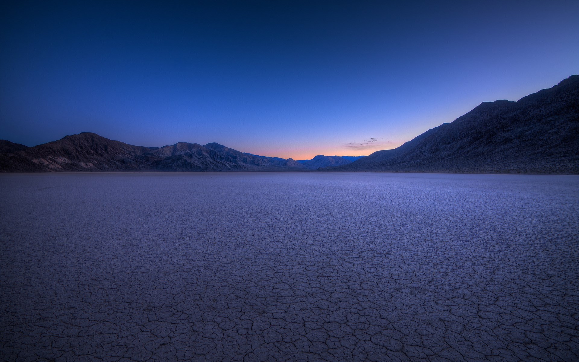 Cracked dry lake bed at dusk with mountains HD Wallpaper