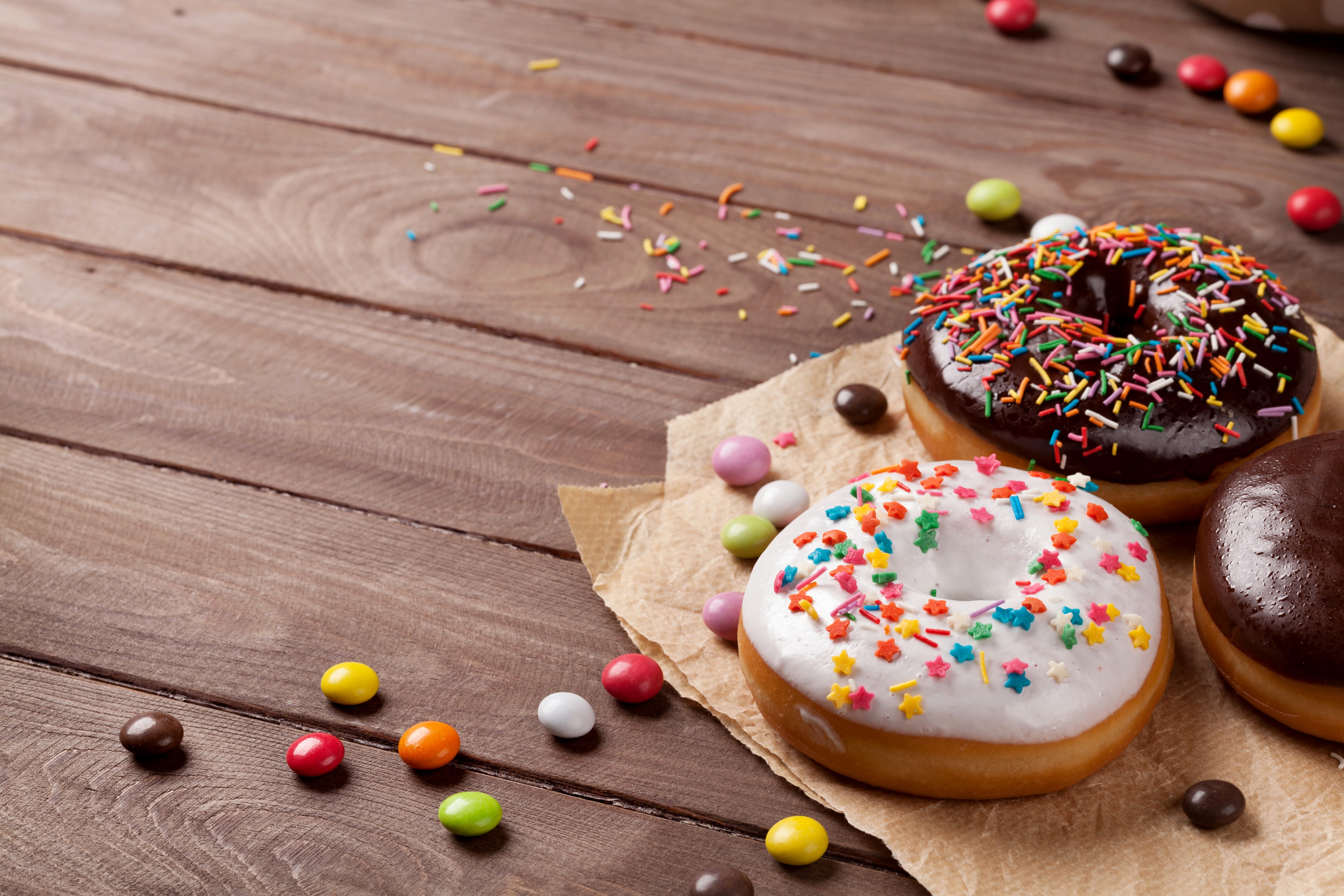 Donuts with chocolate and white icing and sprinkles on wooden planks HD Wallpaper