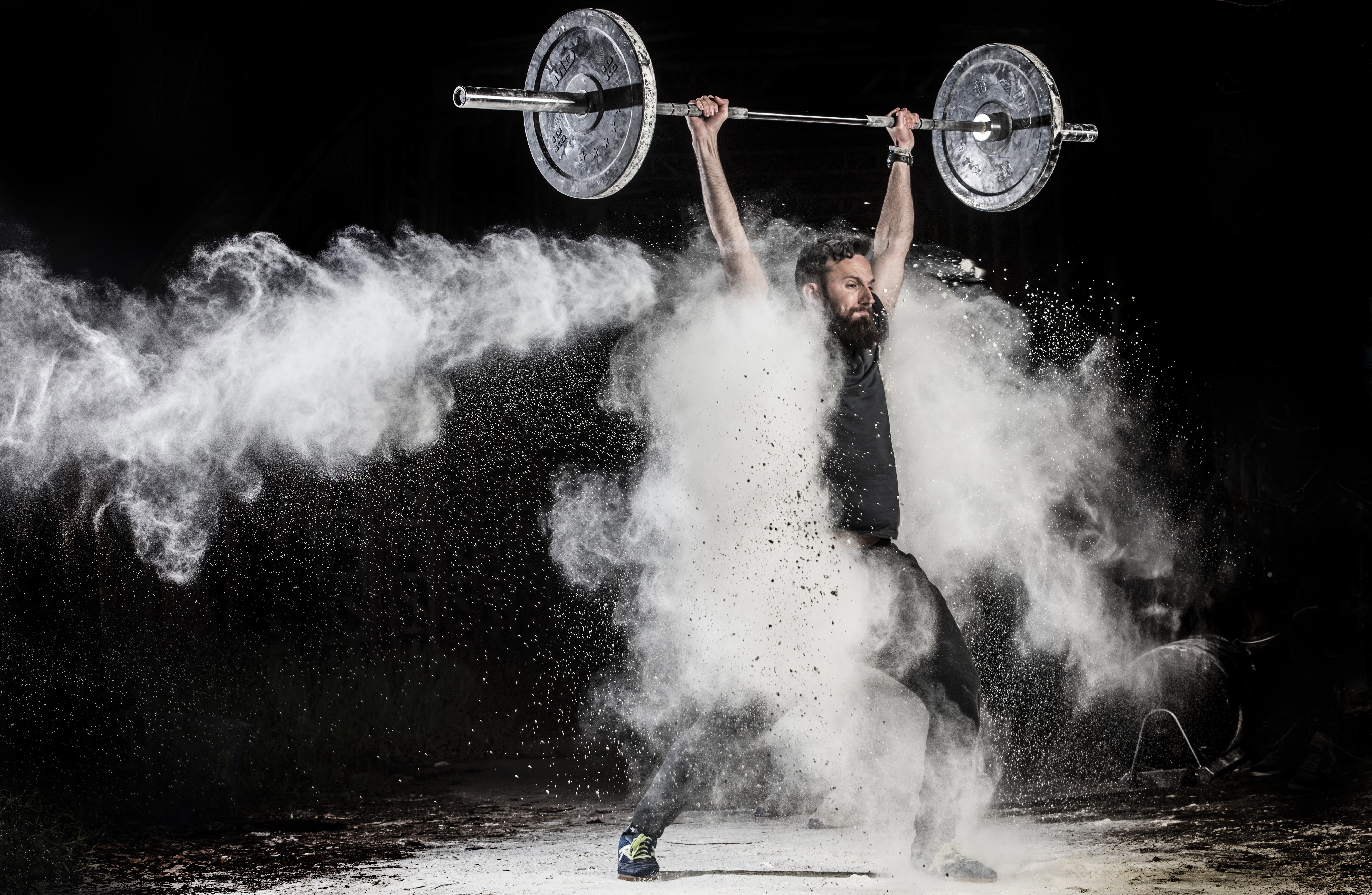 Man lifting barbell with white powder explosion HD Wallpaper