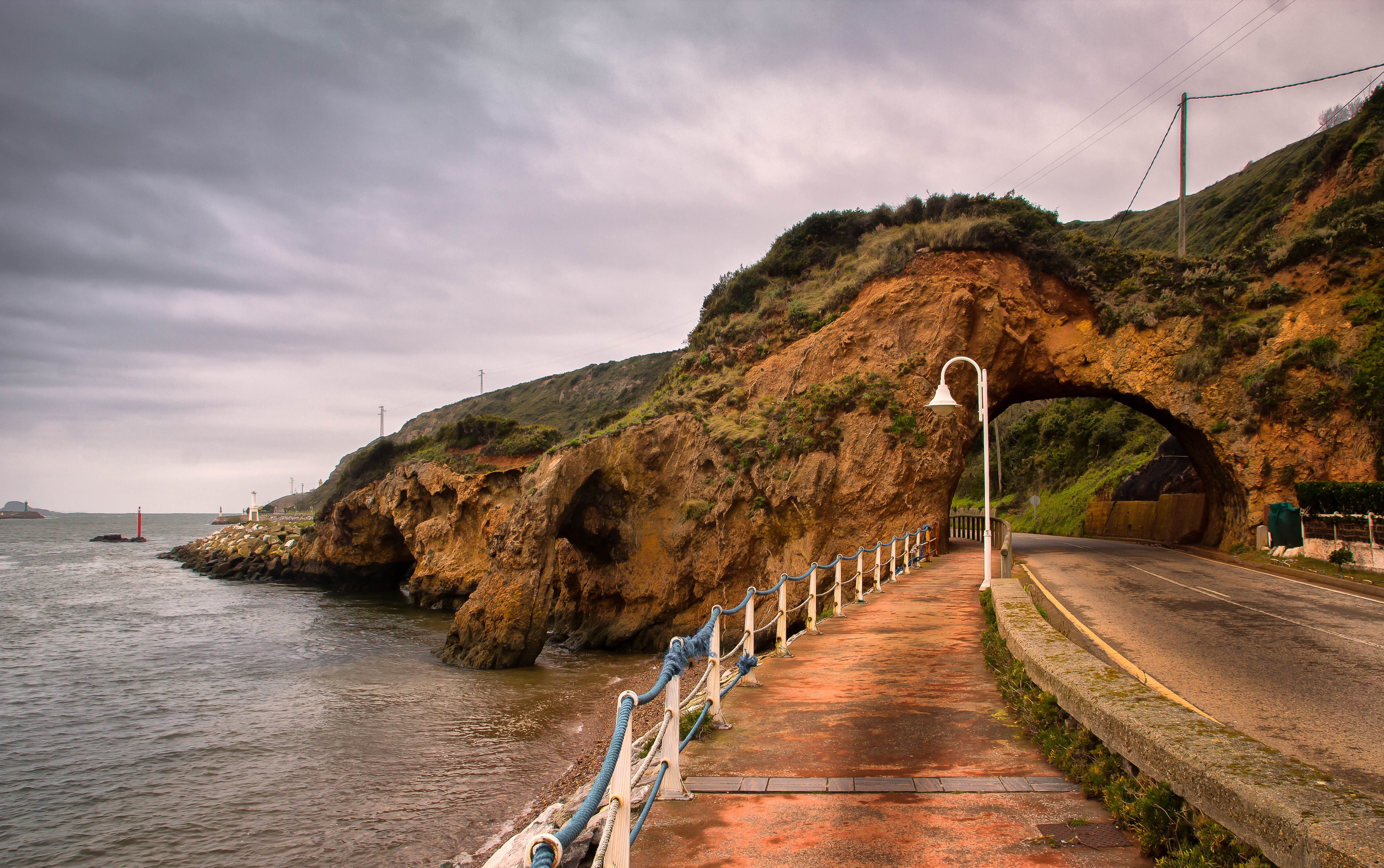 Road through a rock archway on the coast of Aviles Asturias, Spain HD Wallpaper