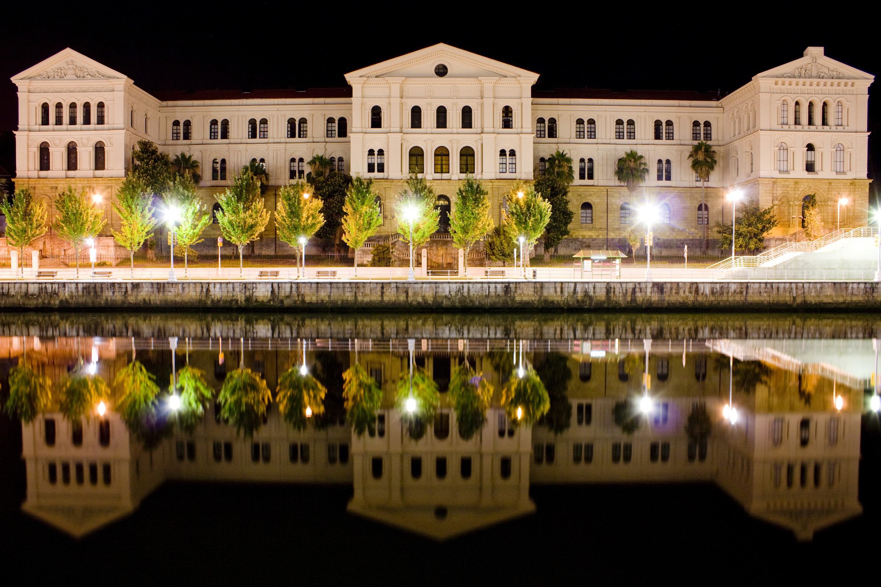 Building and trees reflected in water at night HD Wallpaper
