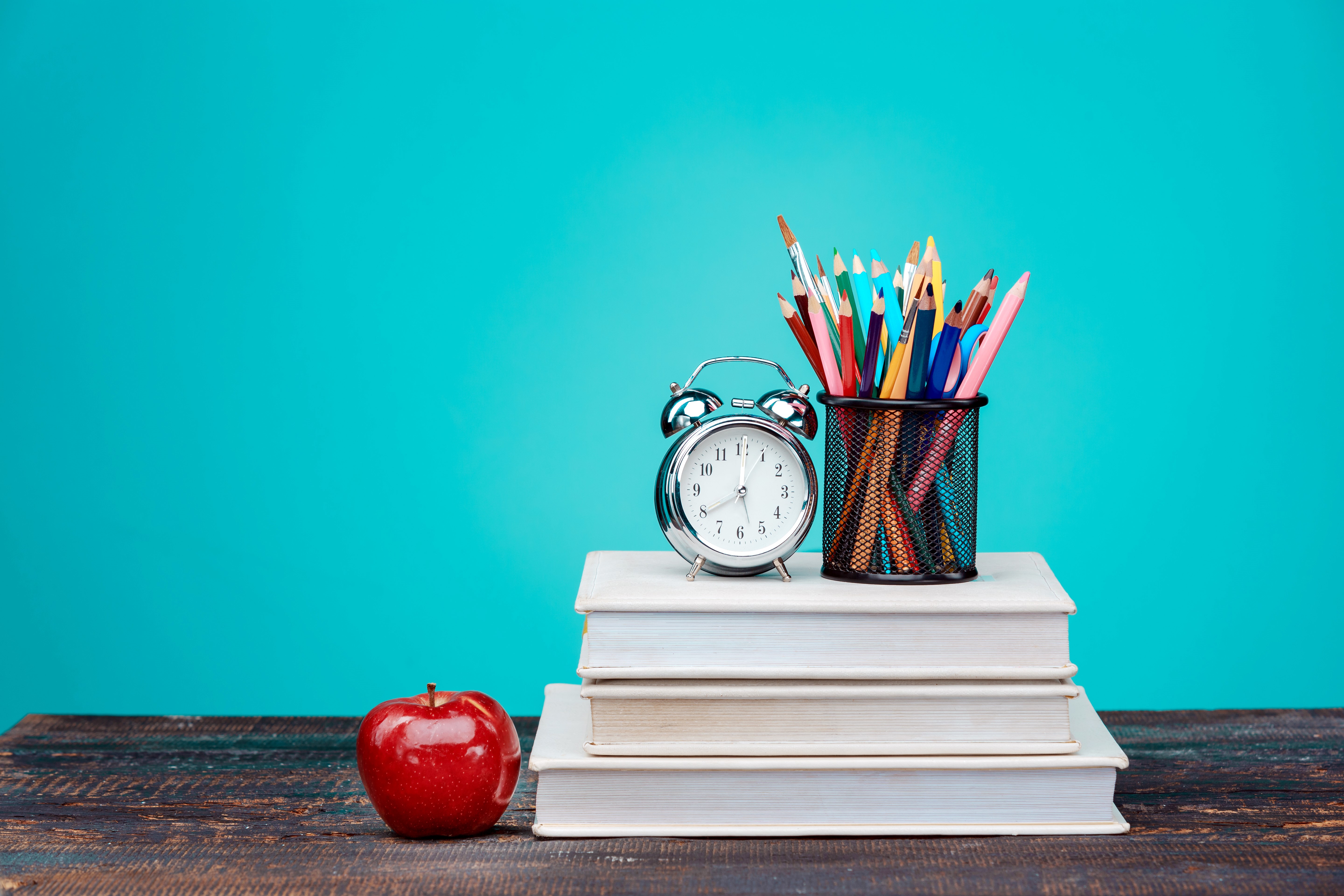 Alarm clock, pencils, books, and apple on a wooden table HD Wallpaper