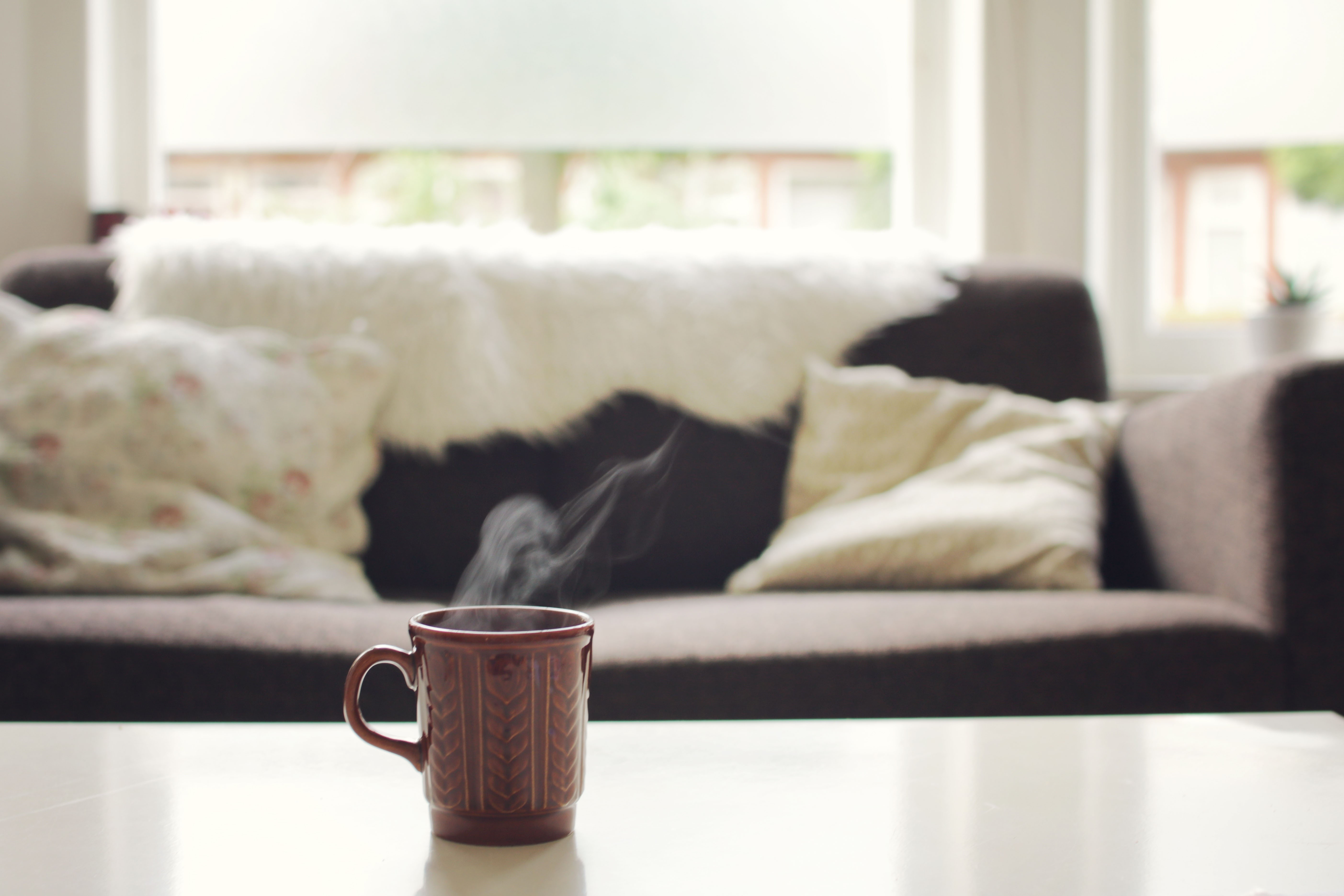 Mug with steam on a table in front of a sofa HD Wallpaper