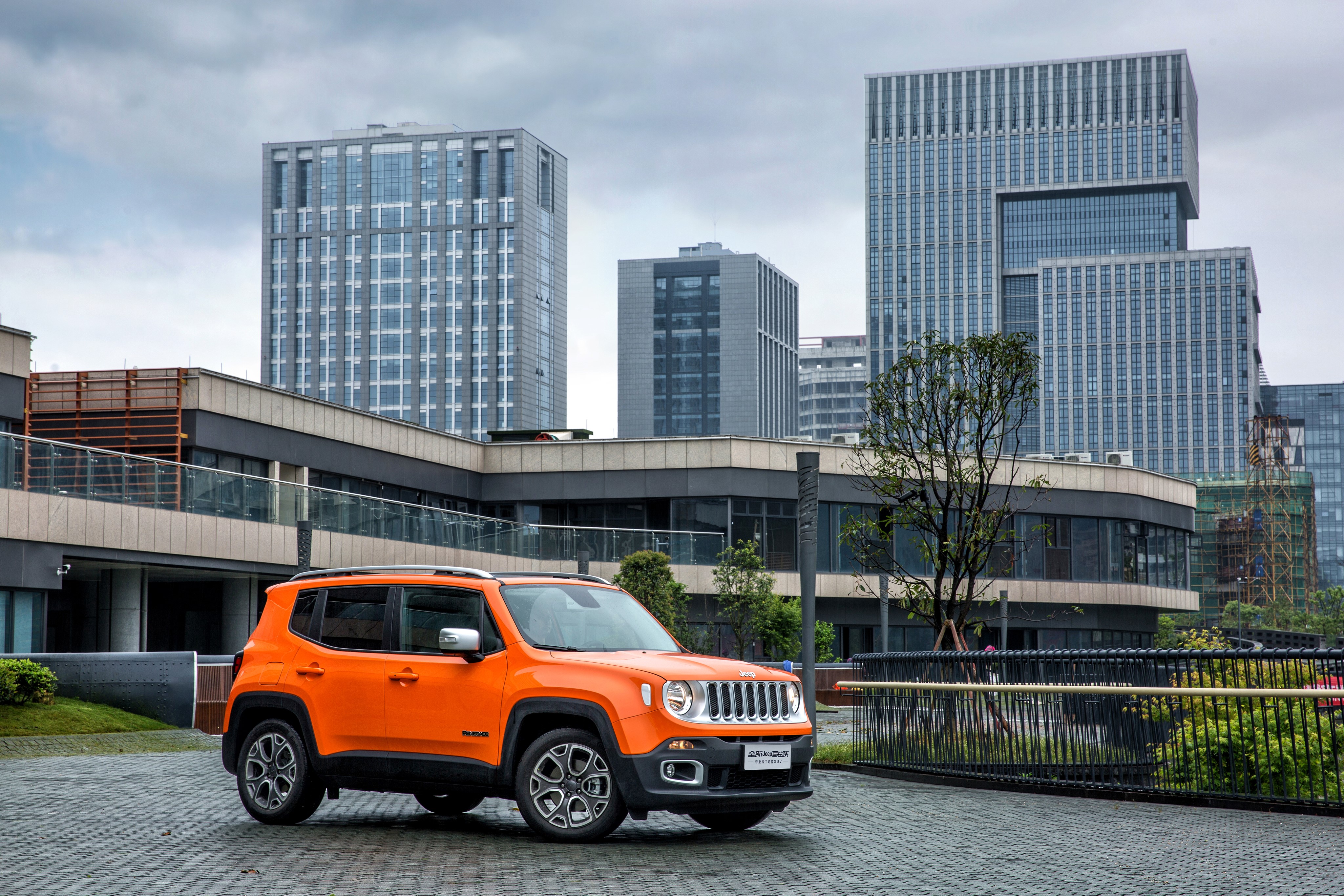 Orange Jeep Renegade Limited in front of modern buildings HD Wallpaper