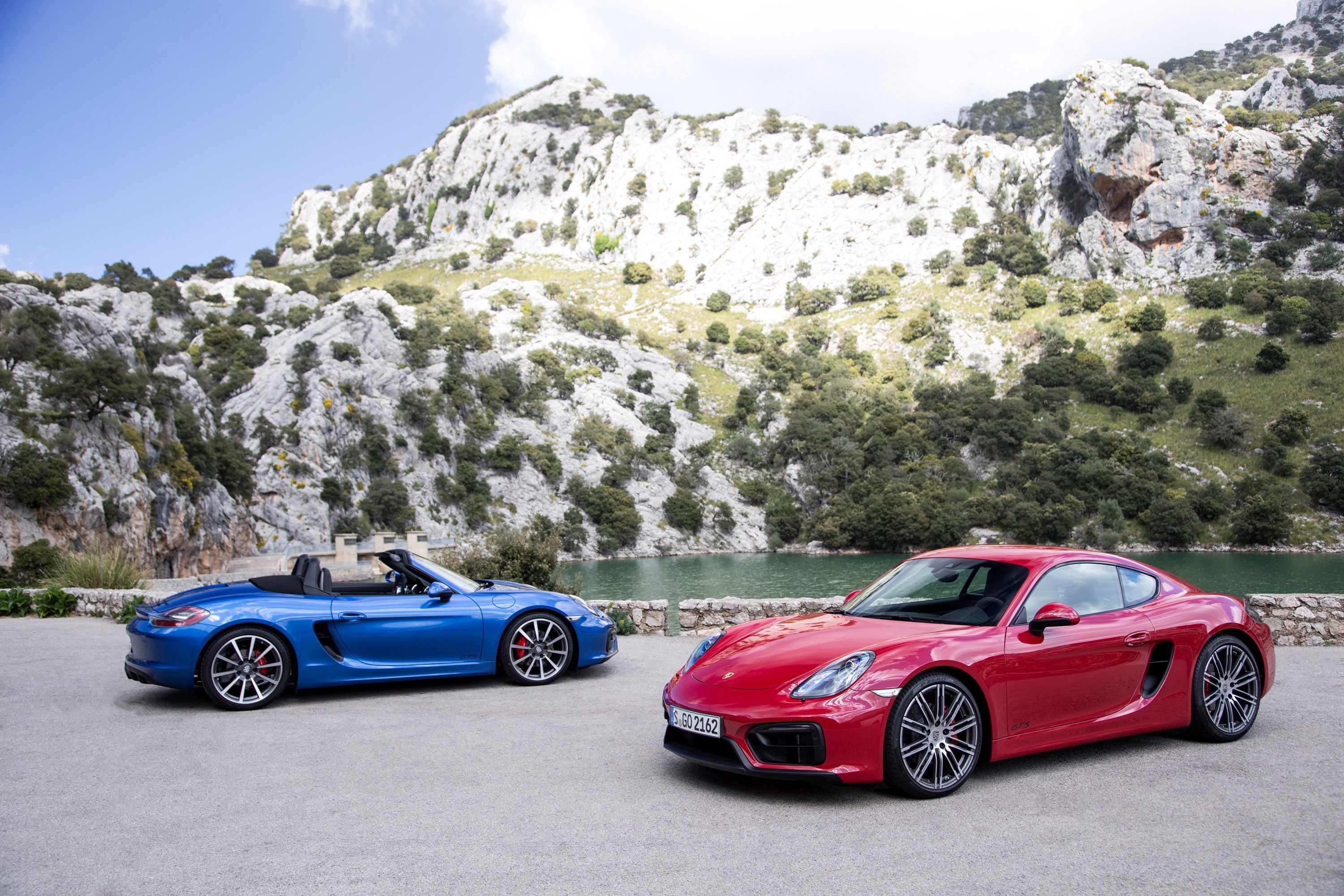 Two Porsche cars, a blue convertible and a red coupe, parked outdoors. HD Wallpaper