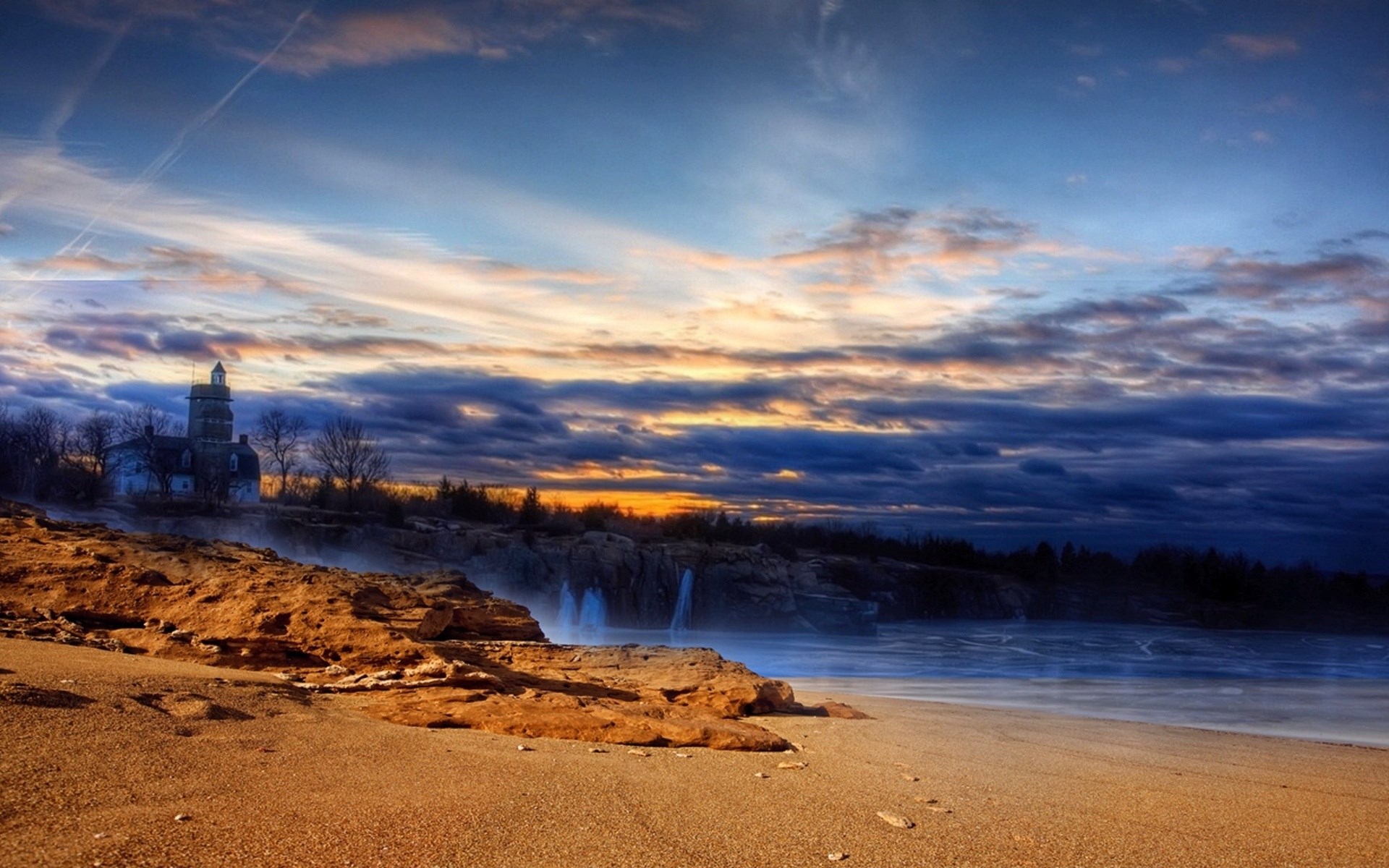 Lighthouse on a rocky coast at sunset HD Wallpaper