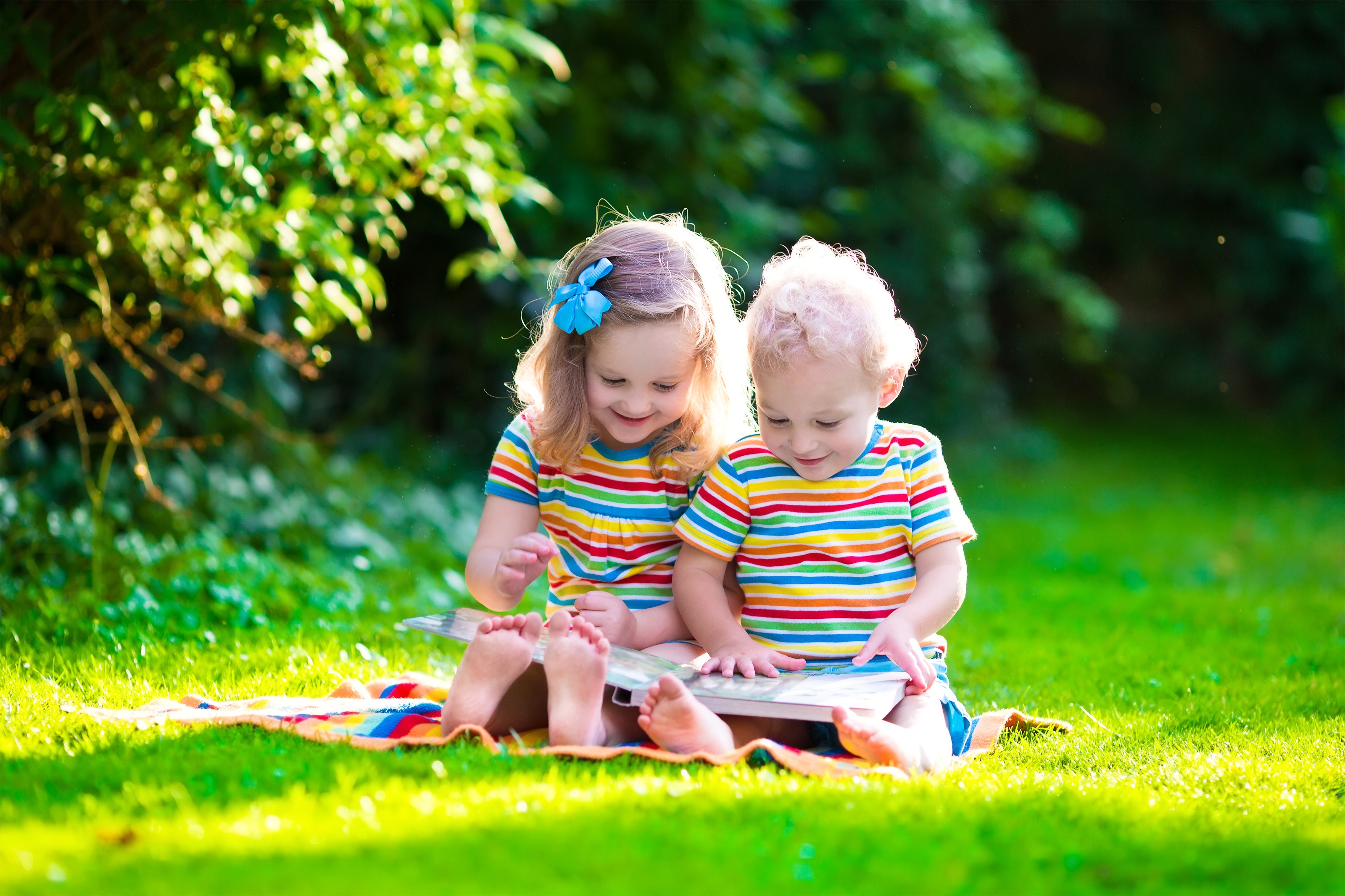 Two children reading a book on the grass HD Wallpaper