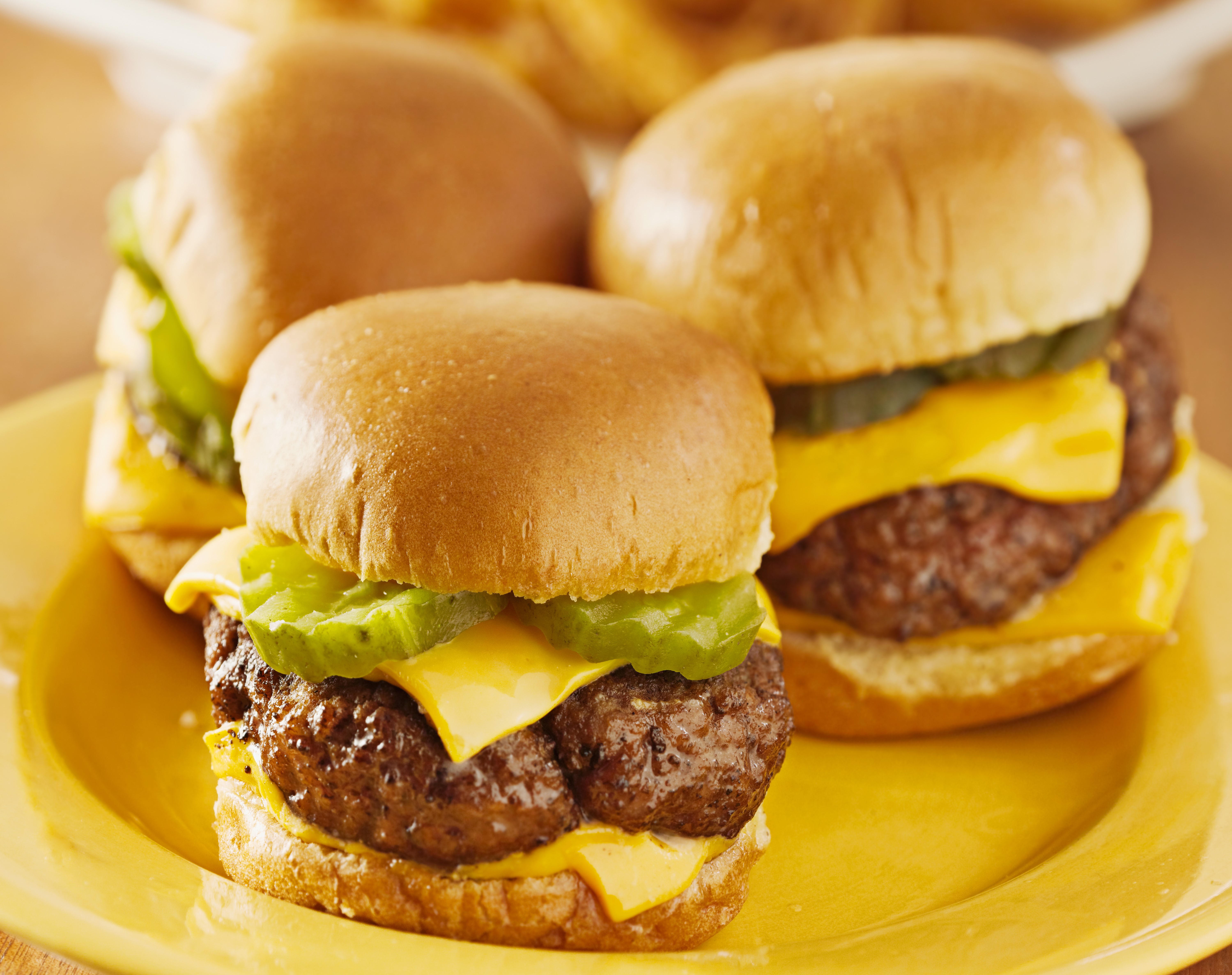 Three cheeseburger sliders with pickles on a yellow plate HD Wallpaper