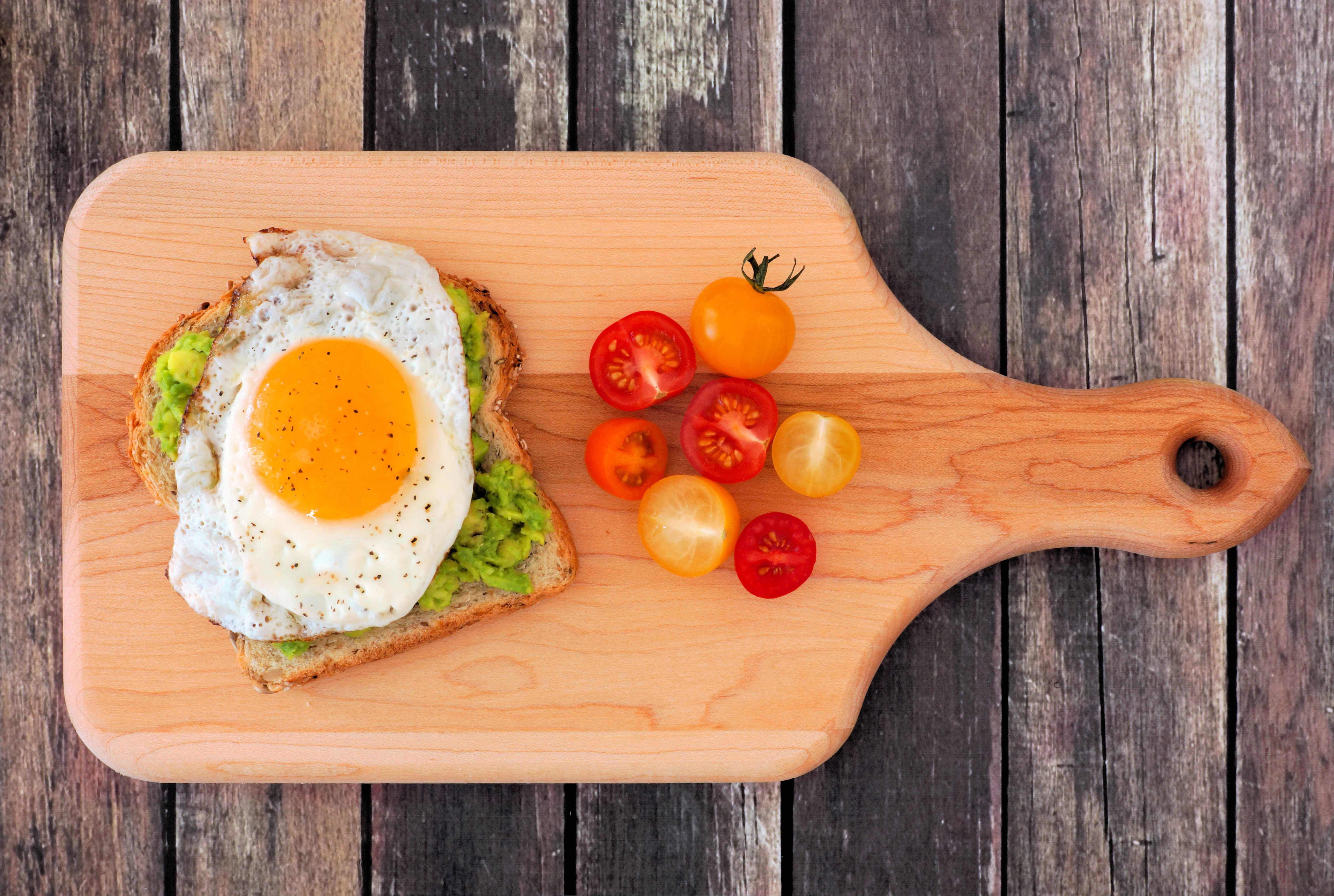 Avocado toast with fried egg and cherry tomatoes on cutting board HD Wallpaper