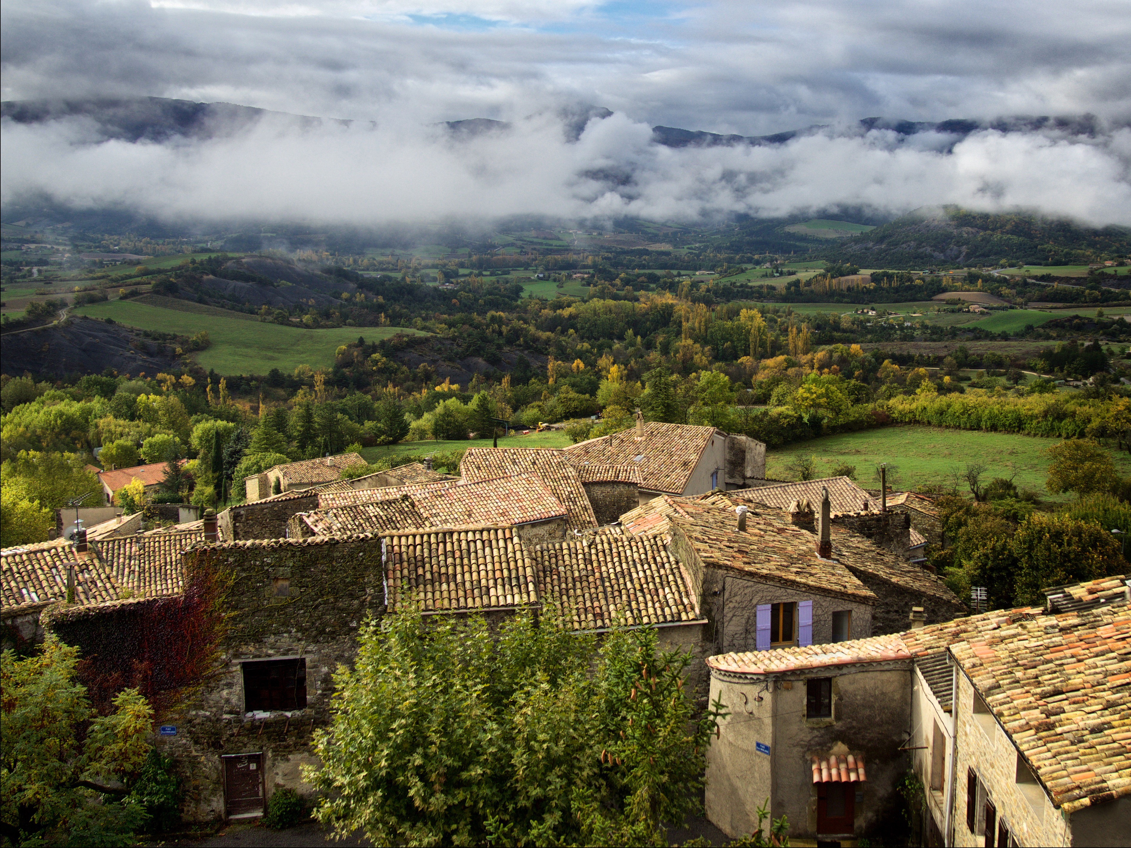 Village rooftops in Rosans, France with misty mountains HD Wallpaper