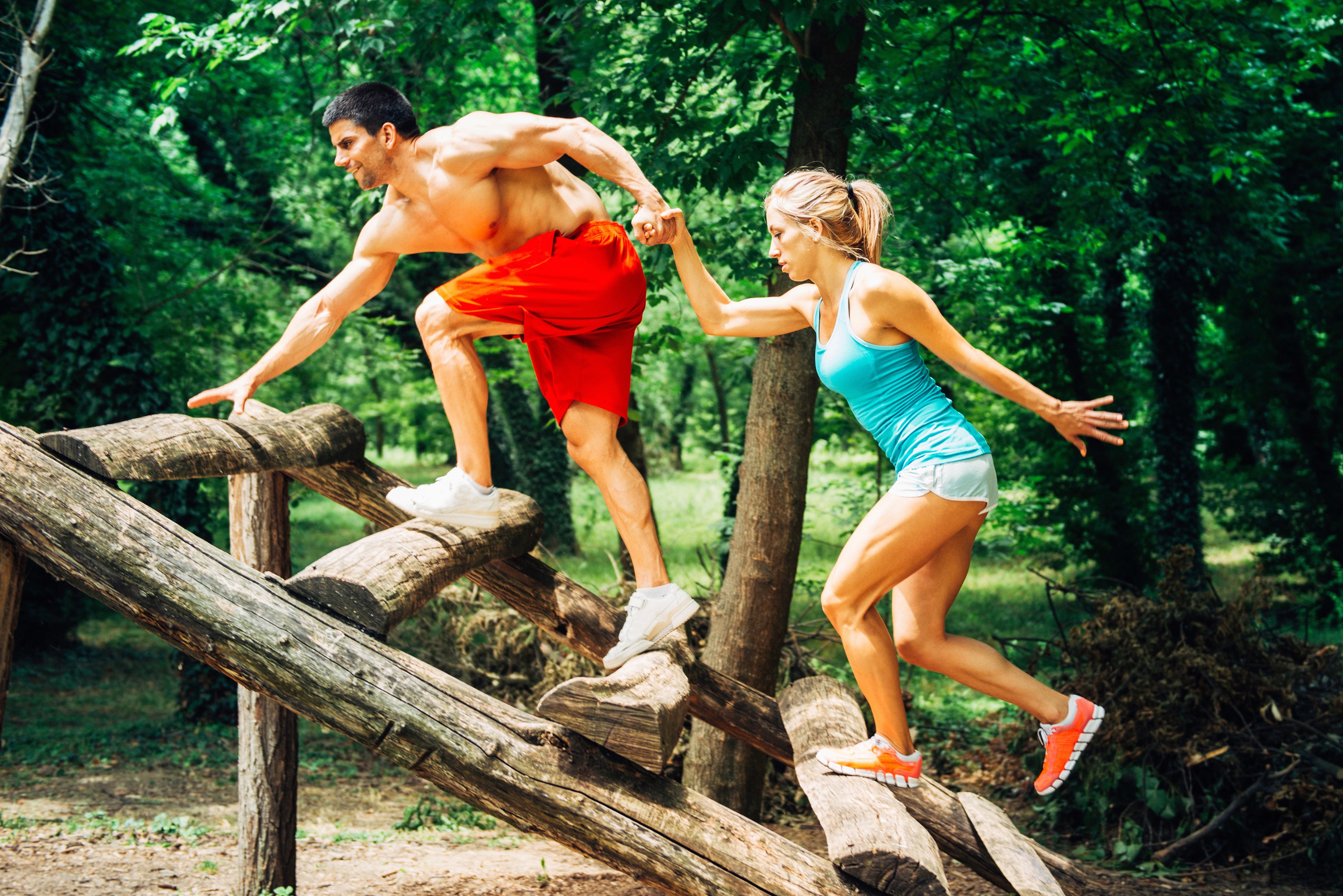 Man and woman doing obstacle course in forest HD Wallpaper