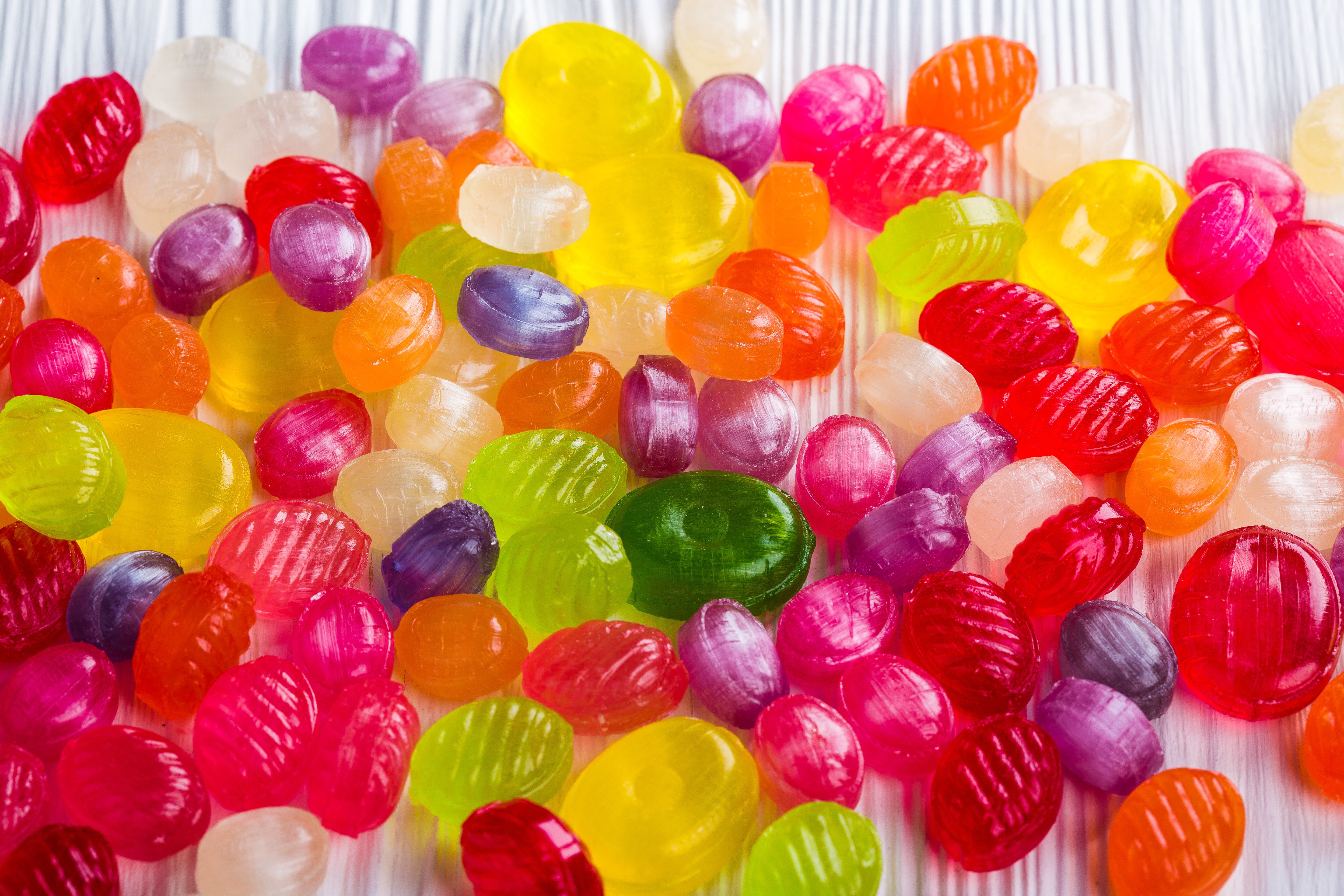 Many colorful candies scattered on a white surface HD Wallpaper
