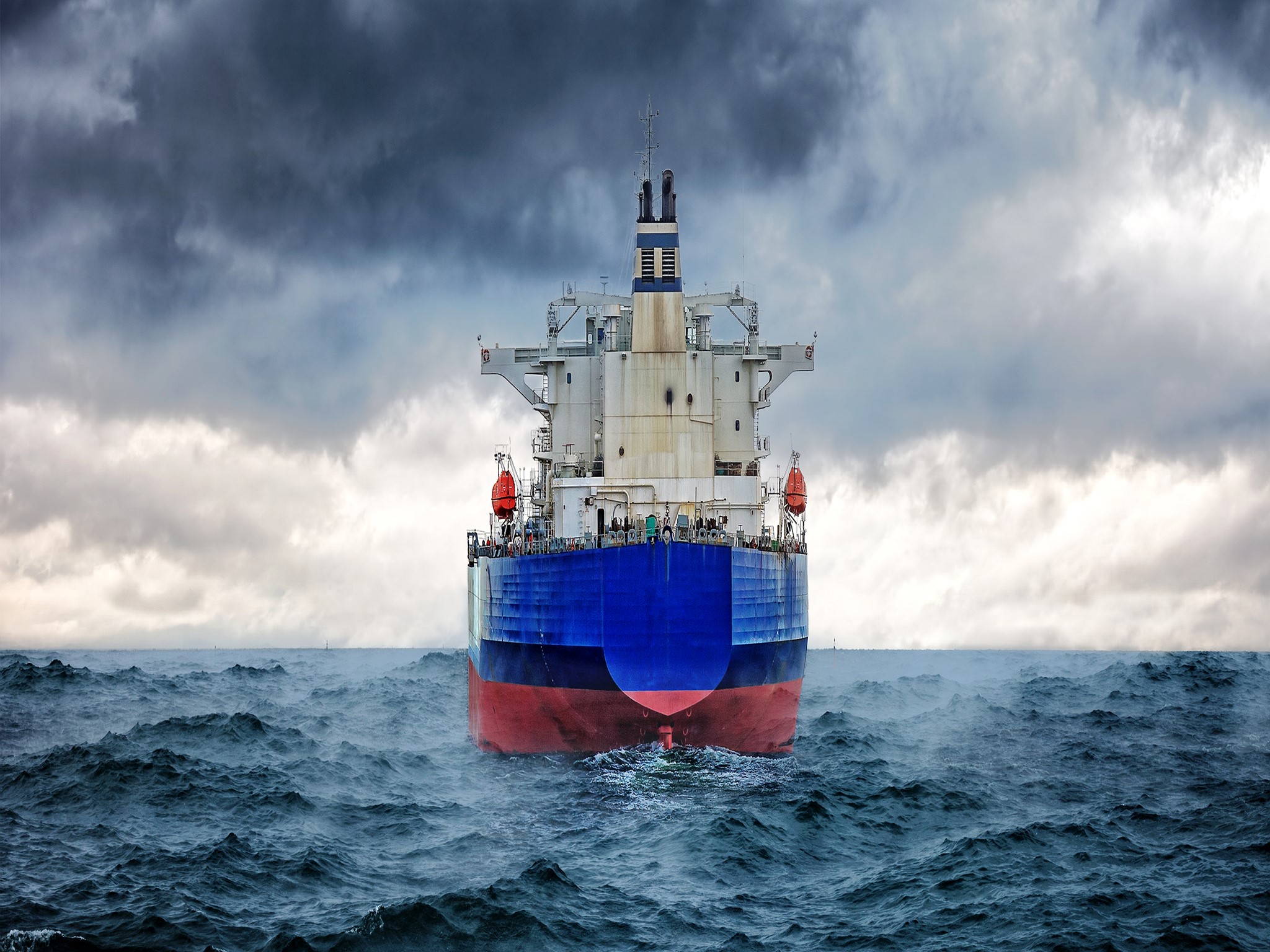A large cargo ship sails through rough seas under stormy clouds HD Wallpaper