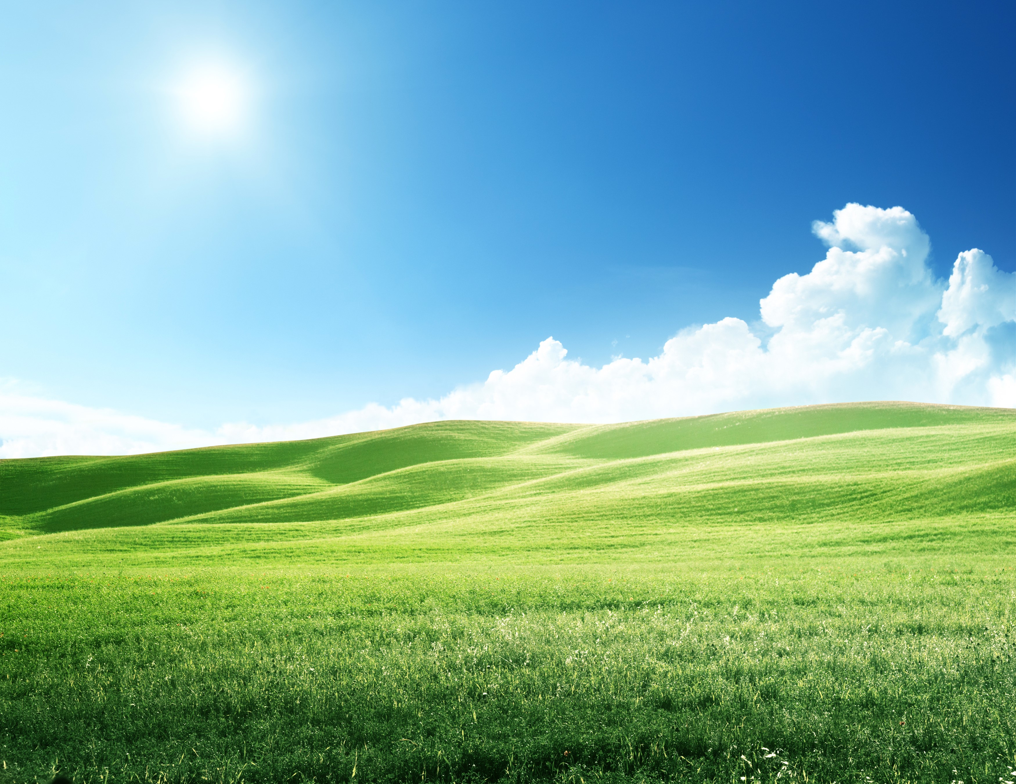 Green rolling hills under a bright blue sky with sun and clouds HD Wallpaper