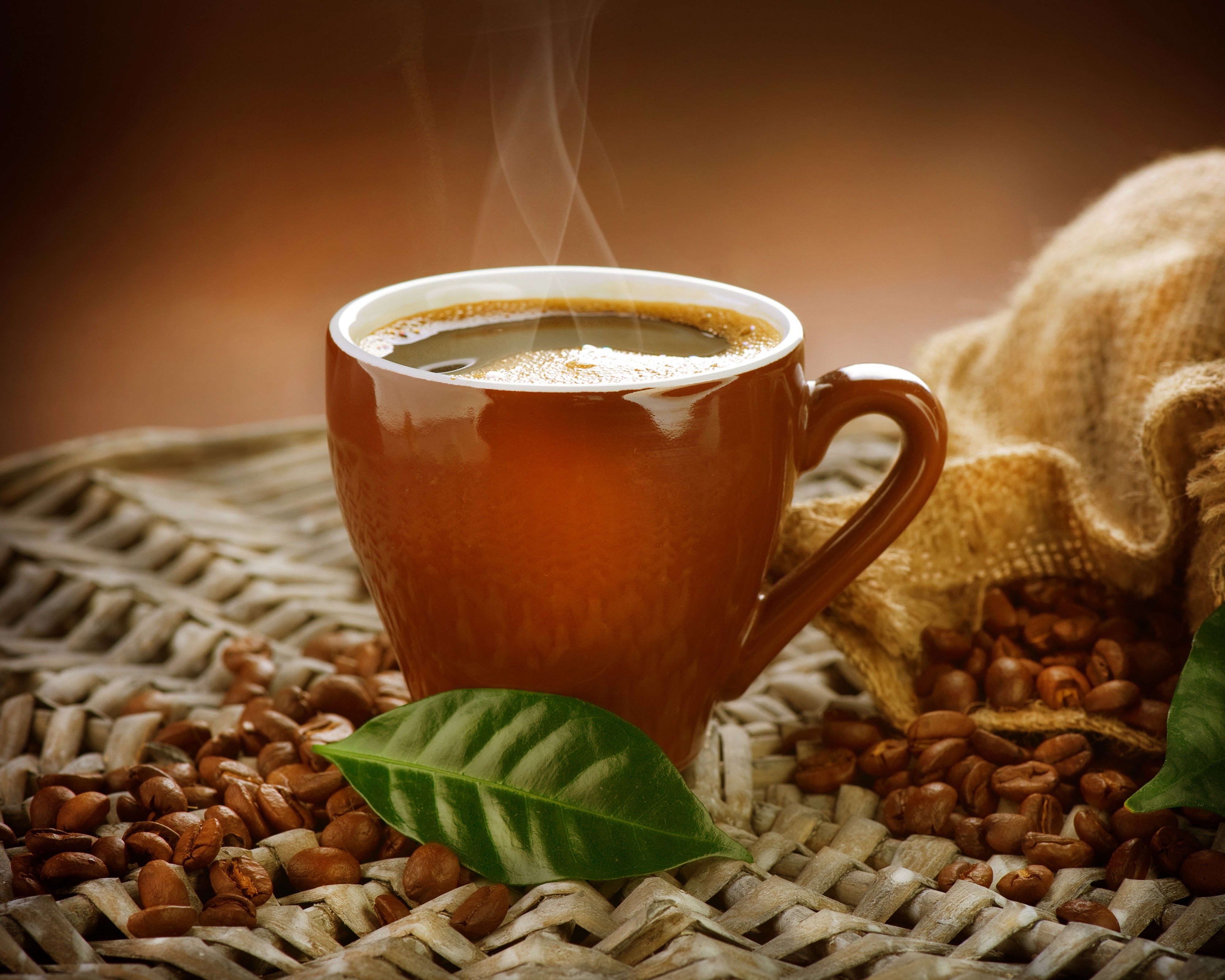 Hot coffee in a brown cup with coffee beans and leaves HD Wallpaper