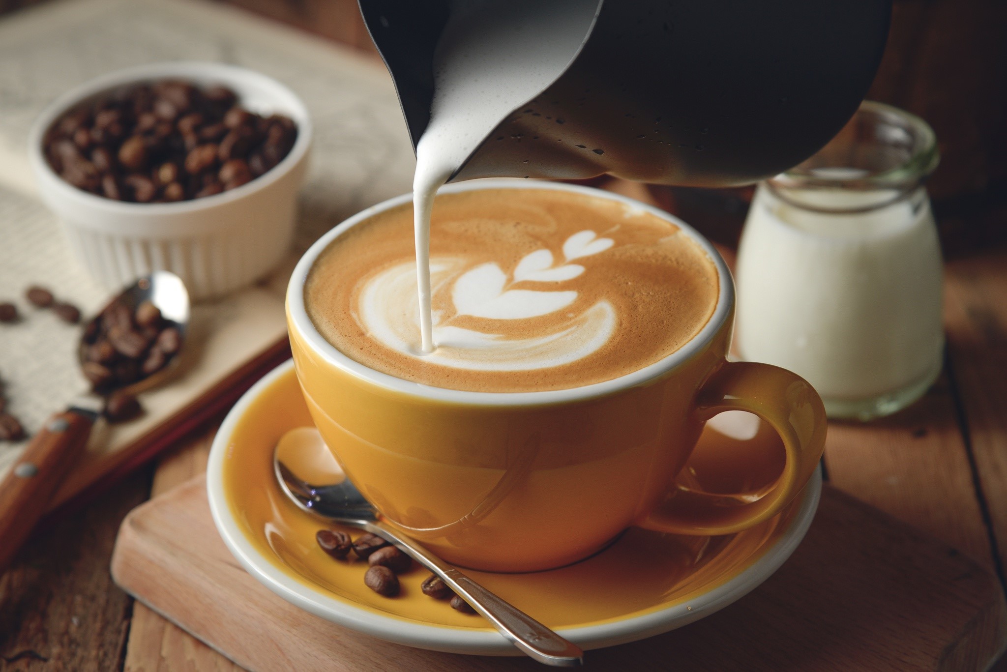Latte art being poured into a yellow cup with coffee beans HD Wallpaper