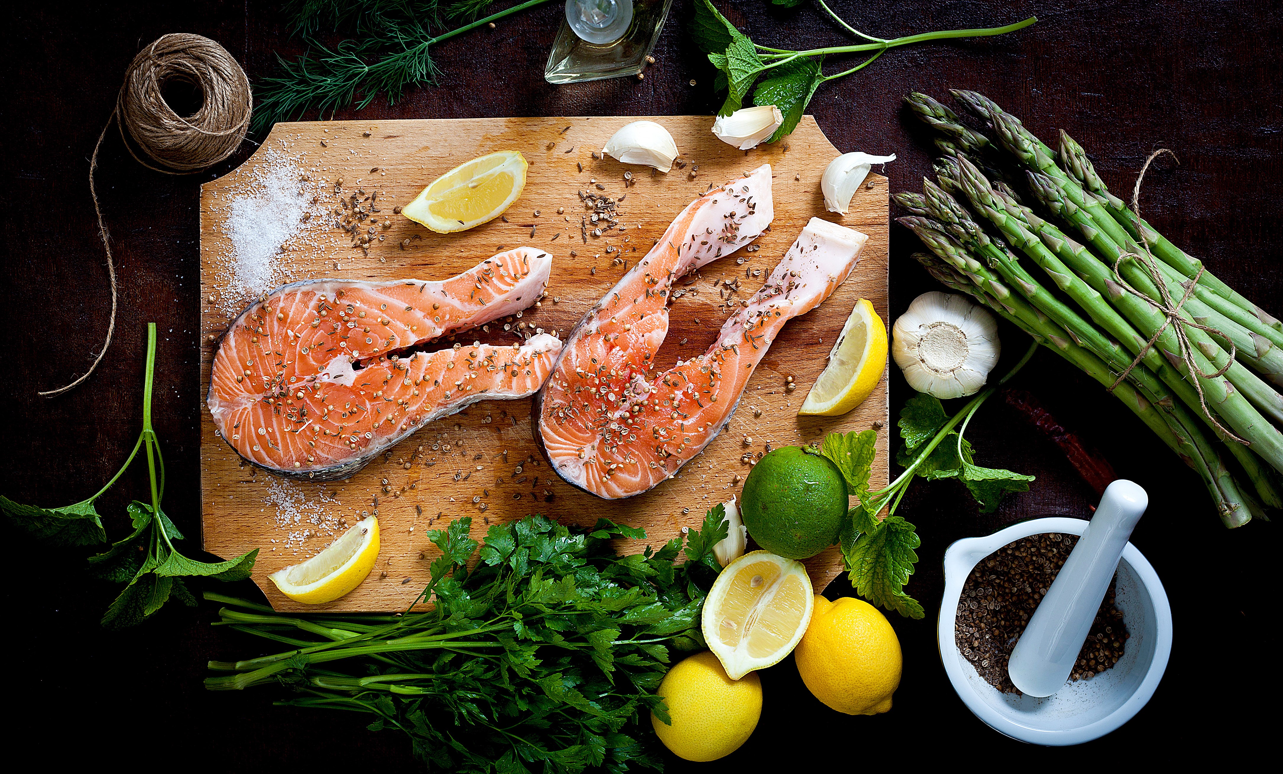 Salmon steaks with asparagus, lemons, garlic, and herbs on a cutting board HD Wallpaper