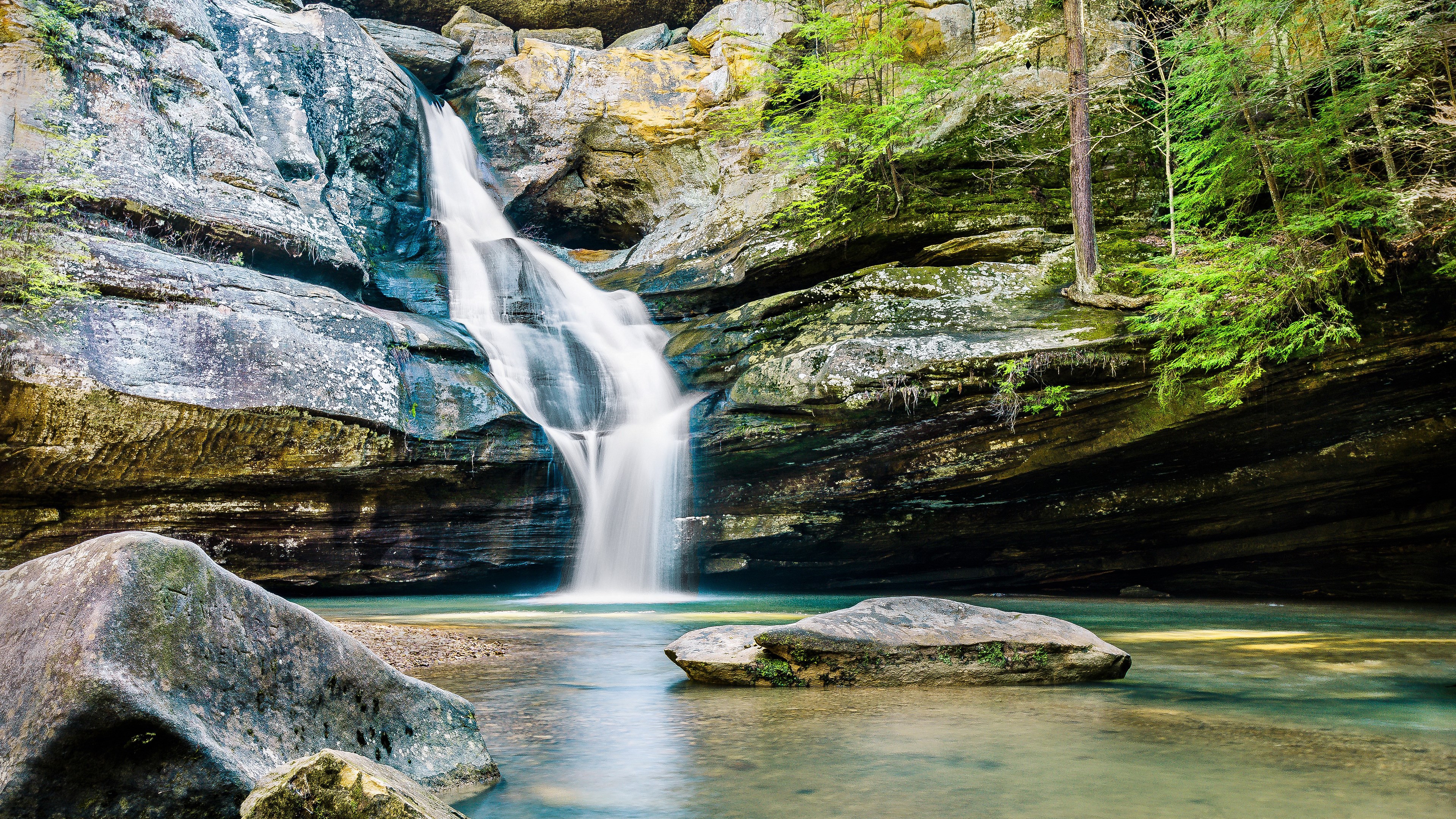 Waterfall cascading over rocks into a pool with trees HD Wallpaper