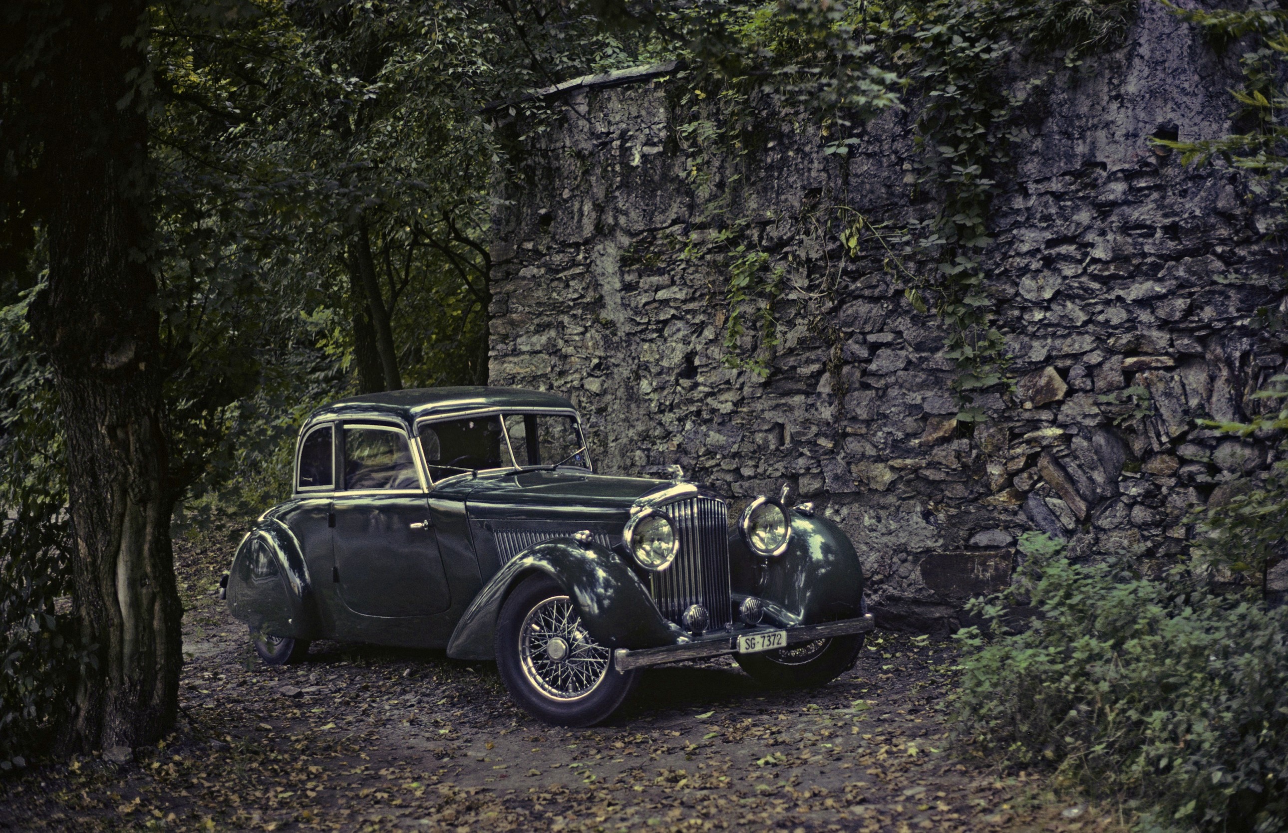 Dark Green Bentley parked by a stone wall HD Wallpaper