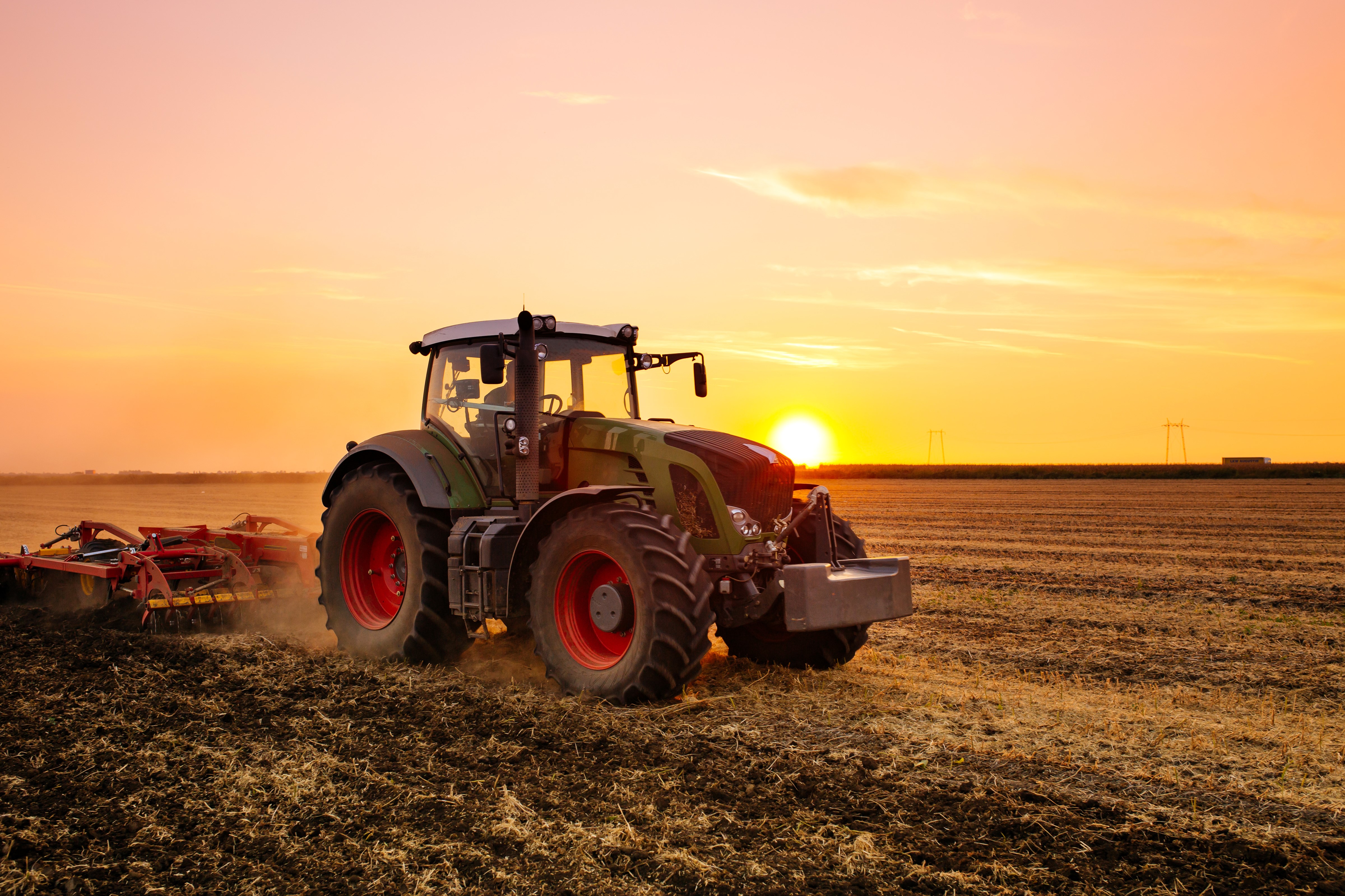 Tractor plowing a field at sunset HD Wallpaper