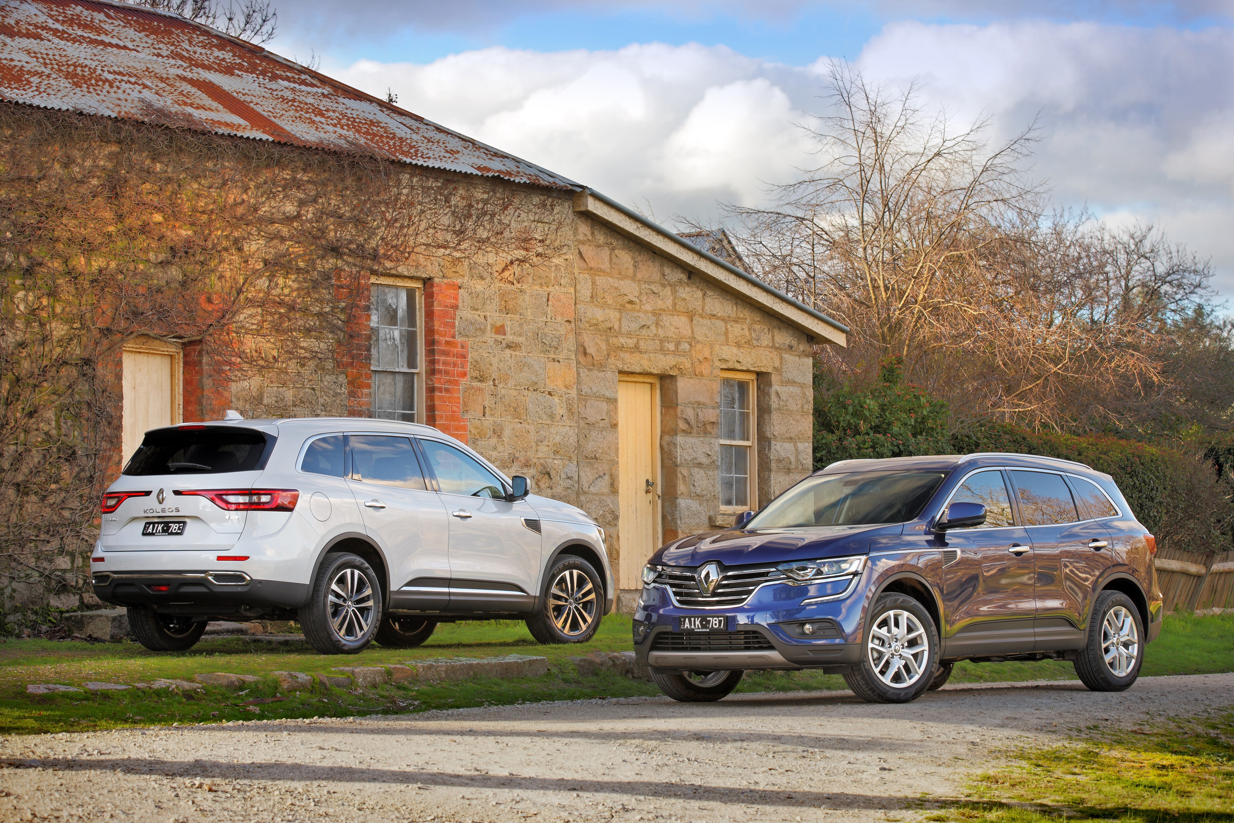 Two Renault Koleos cars parked near a stone building HD Wallpaper