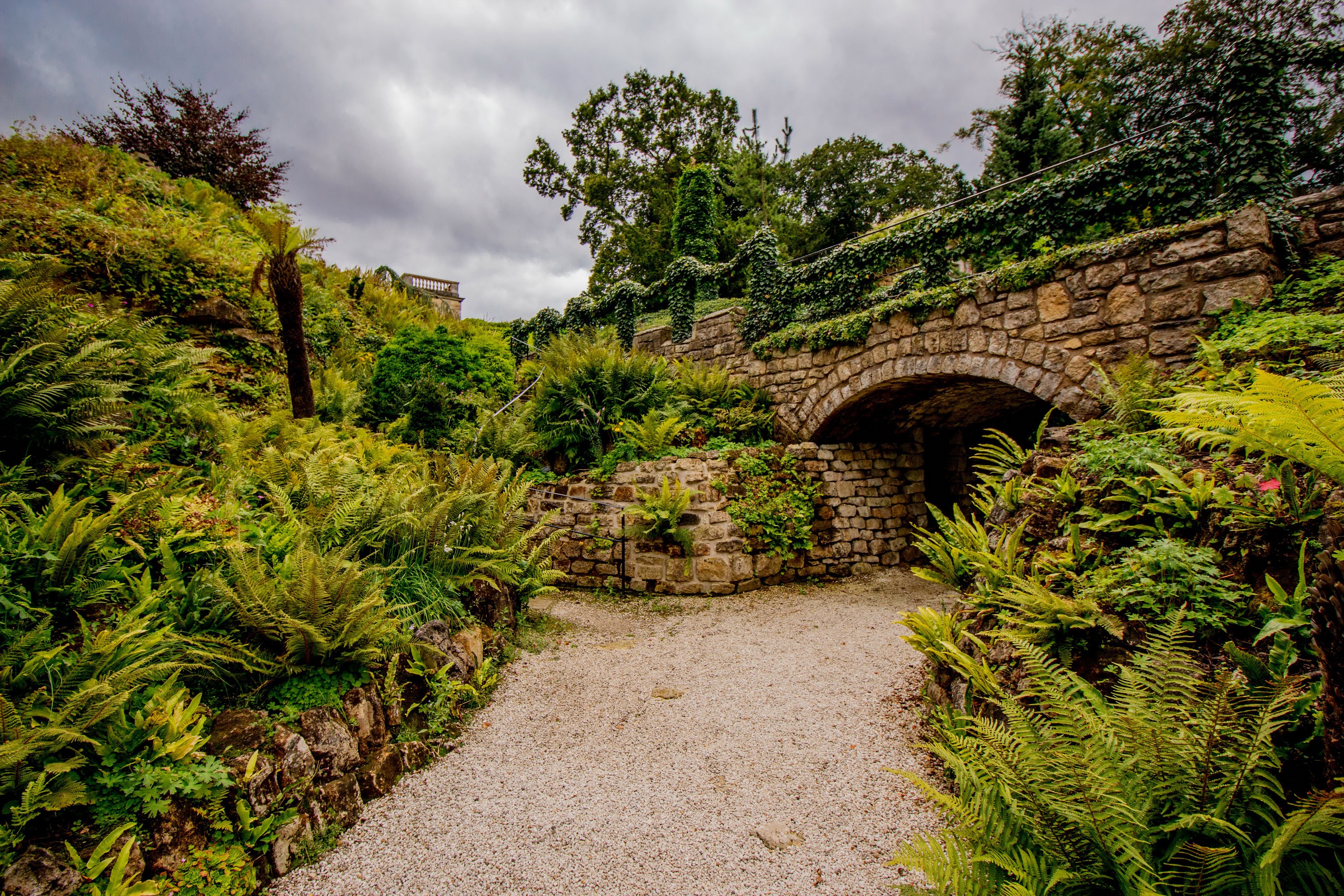 Stone bridge over a path in a garden with ferns HD Wallpaper
