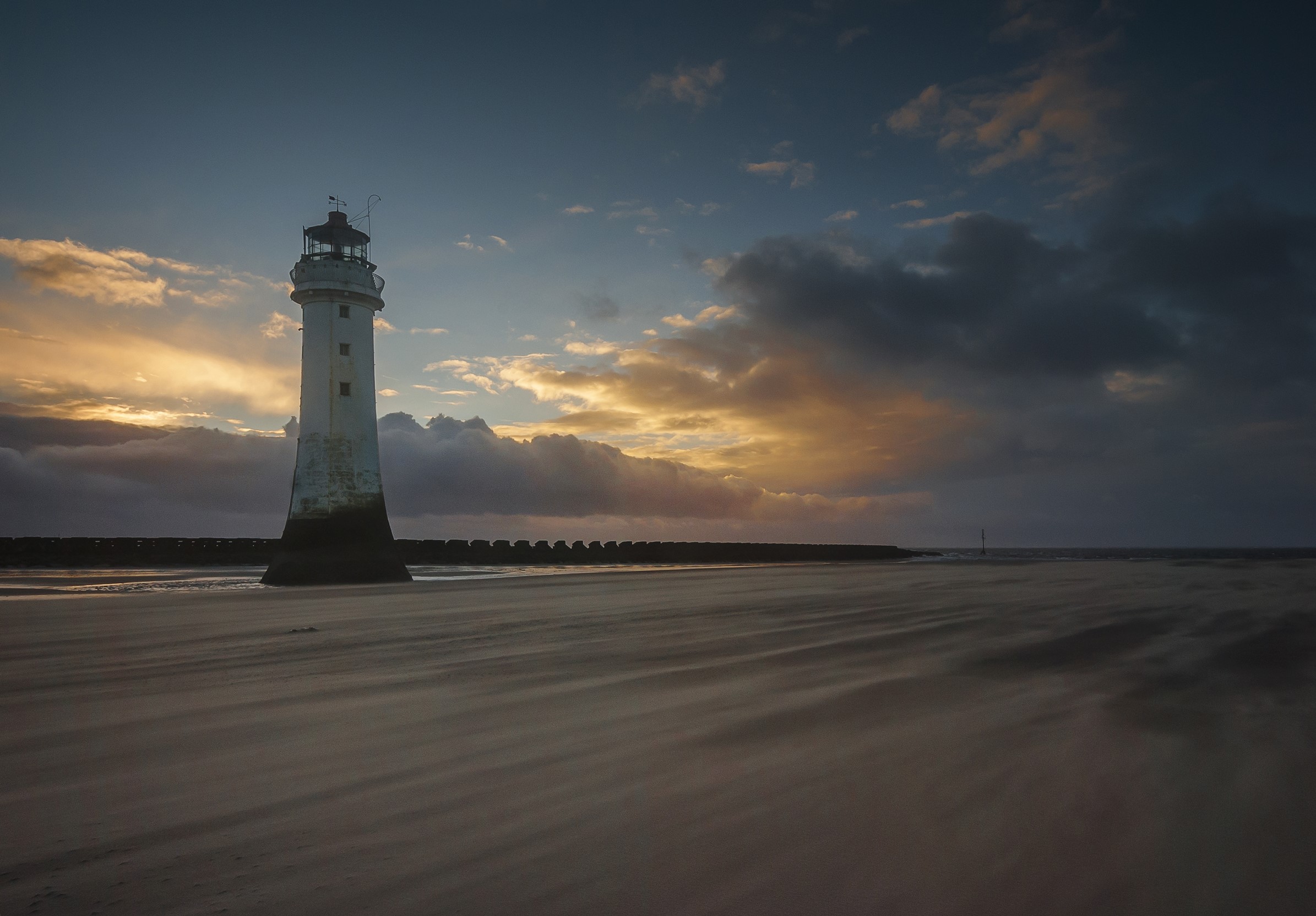 Lighthouse on a beach at sunset with dramatic clouds HD Wallpaper