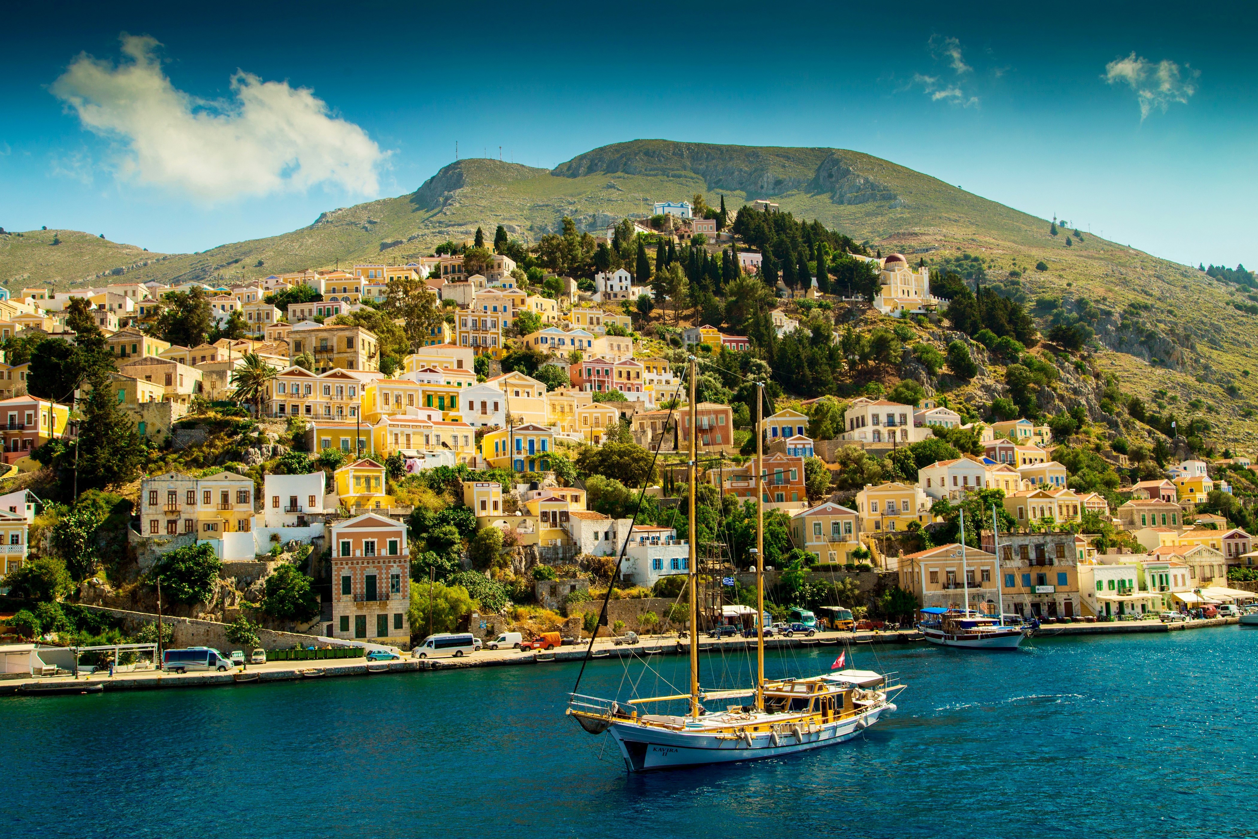 Sailing yacht in a bay with houses on a hill in Symi, Greece HD Wallpaper