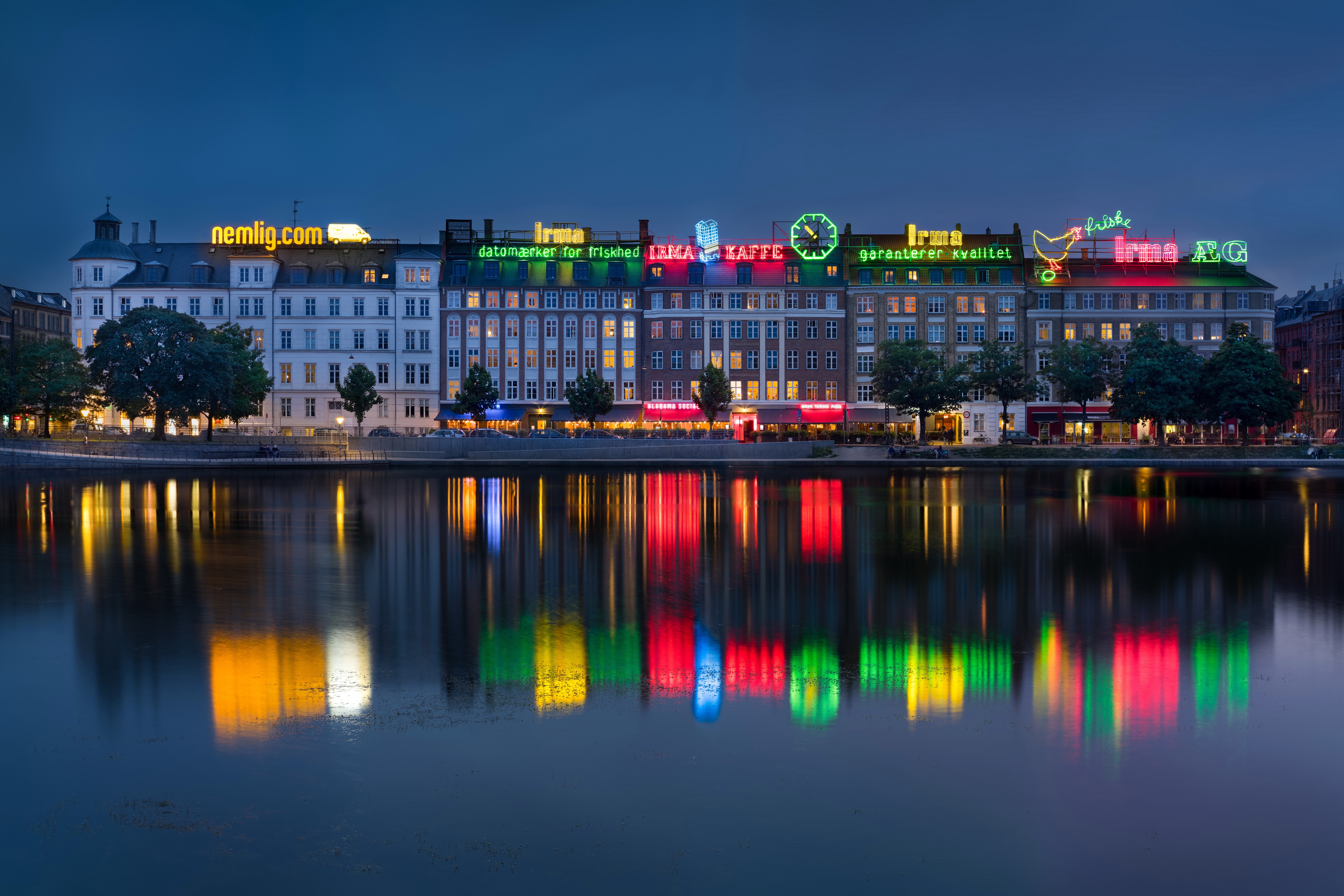 Copenhagen buildings with neon signs reflected in water at dusk HD Wallpaper