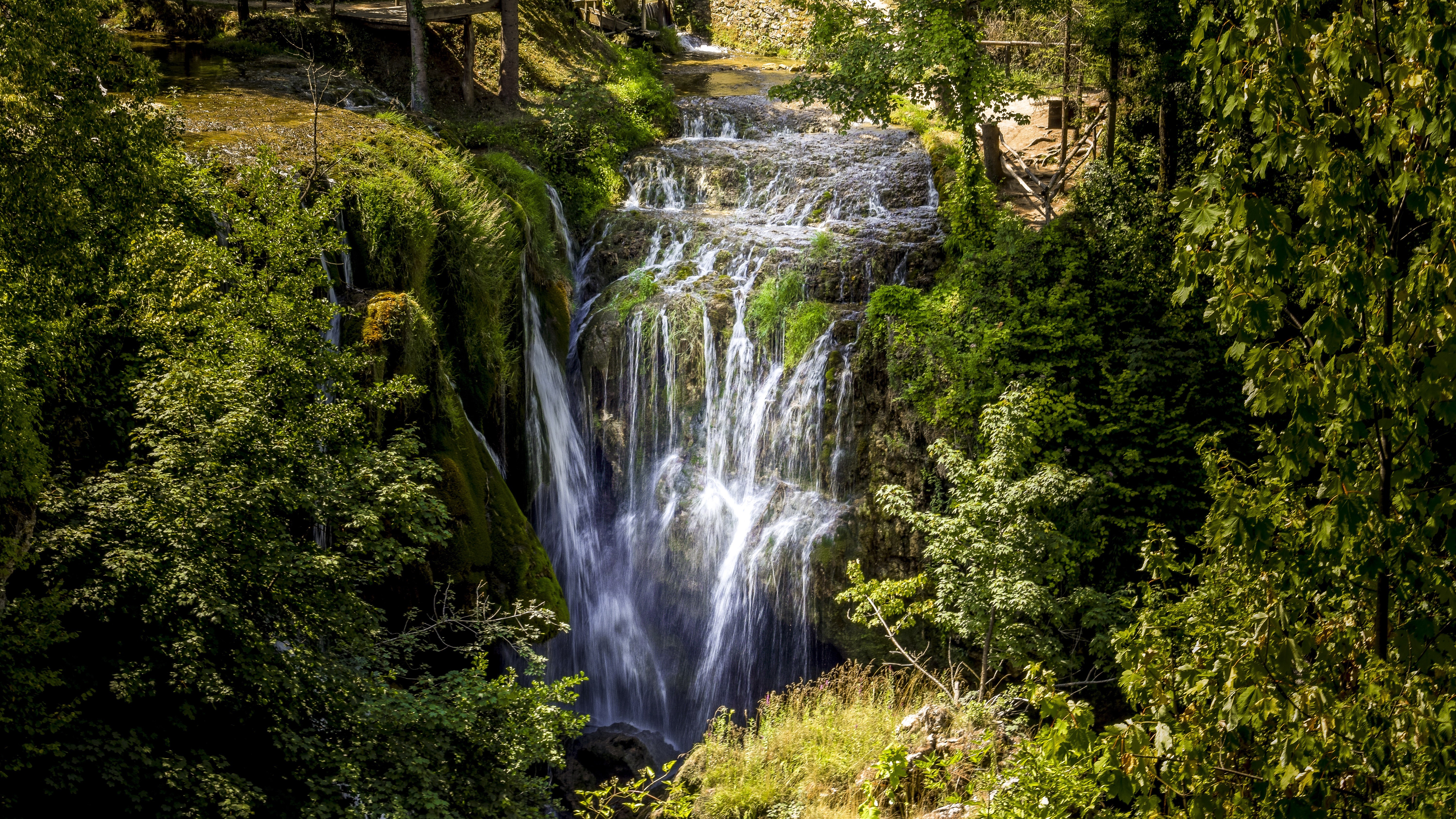 Waterfalls cascading down a mossy crag surrounded by trees HD Wallpaper