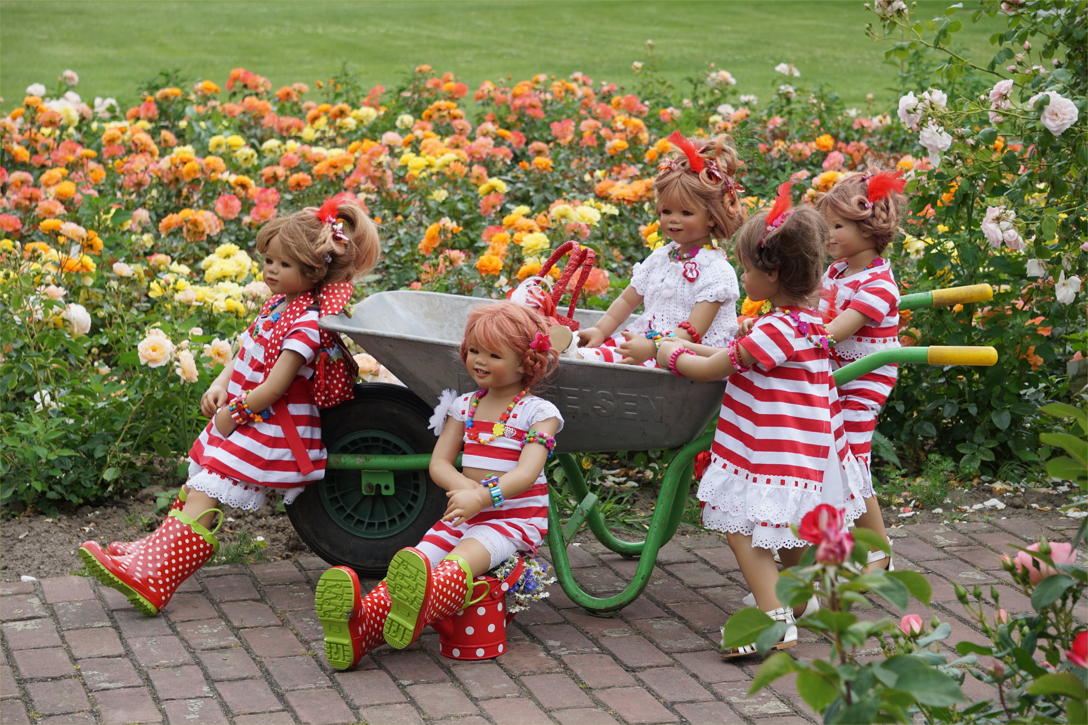 Dolls in a garden with roses and a wheelbarrow HD Wallpaper