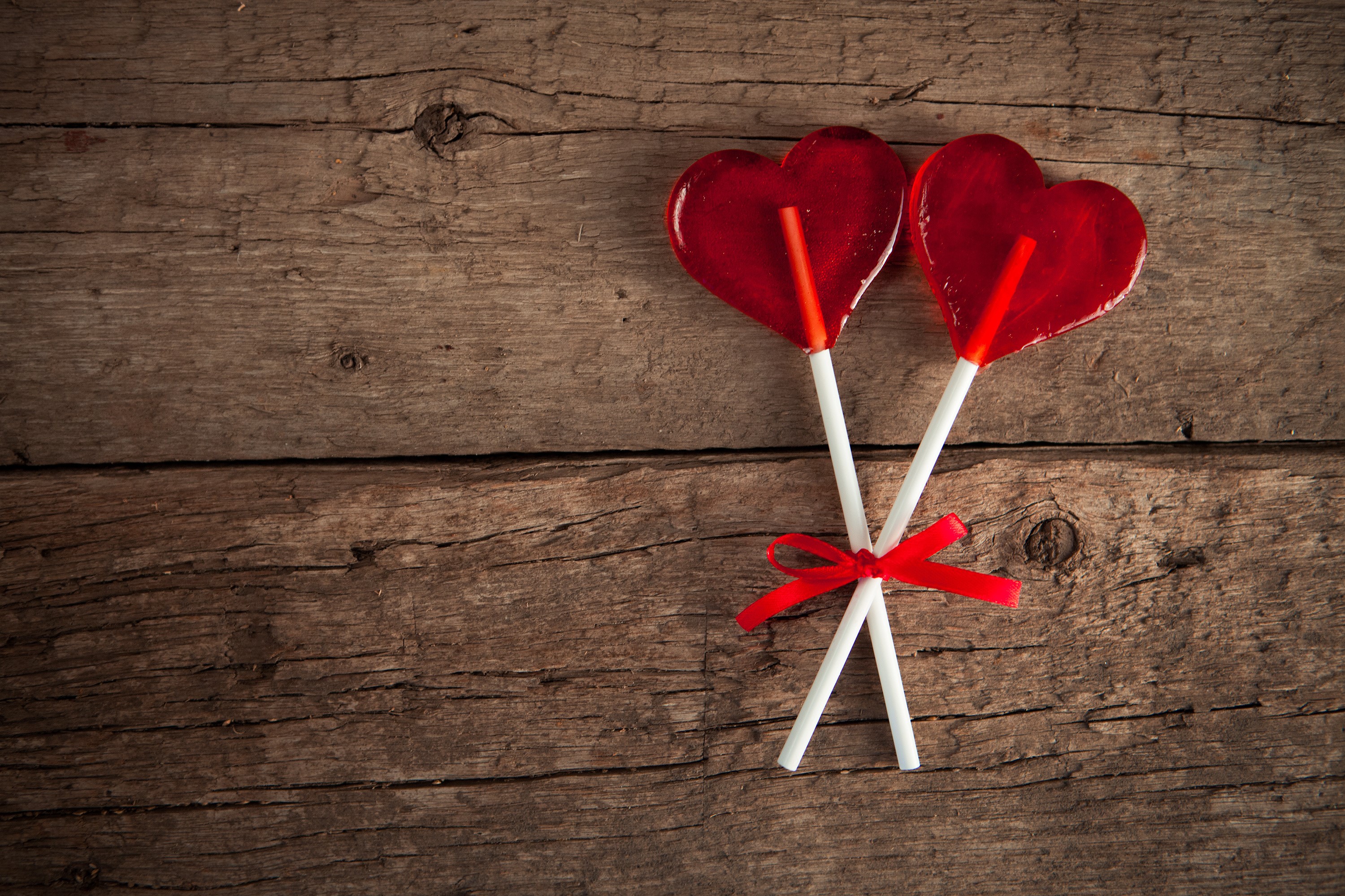 Two red heart lollipops tied with a red ribbon on wood planks HD Wallpaper