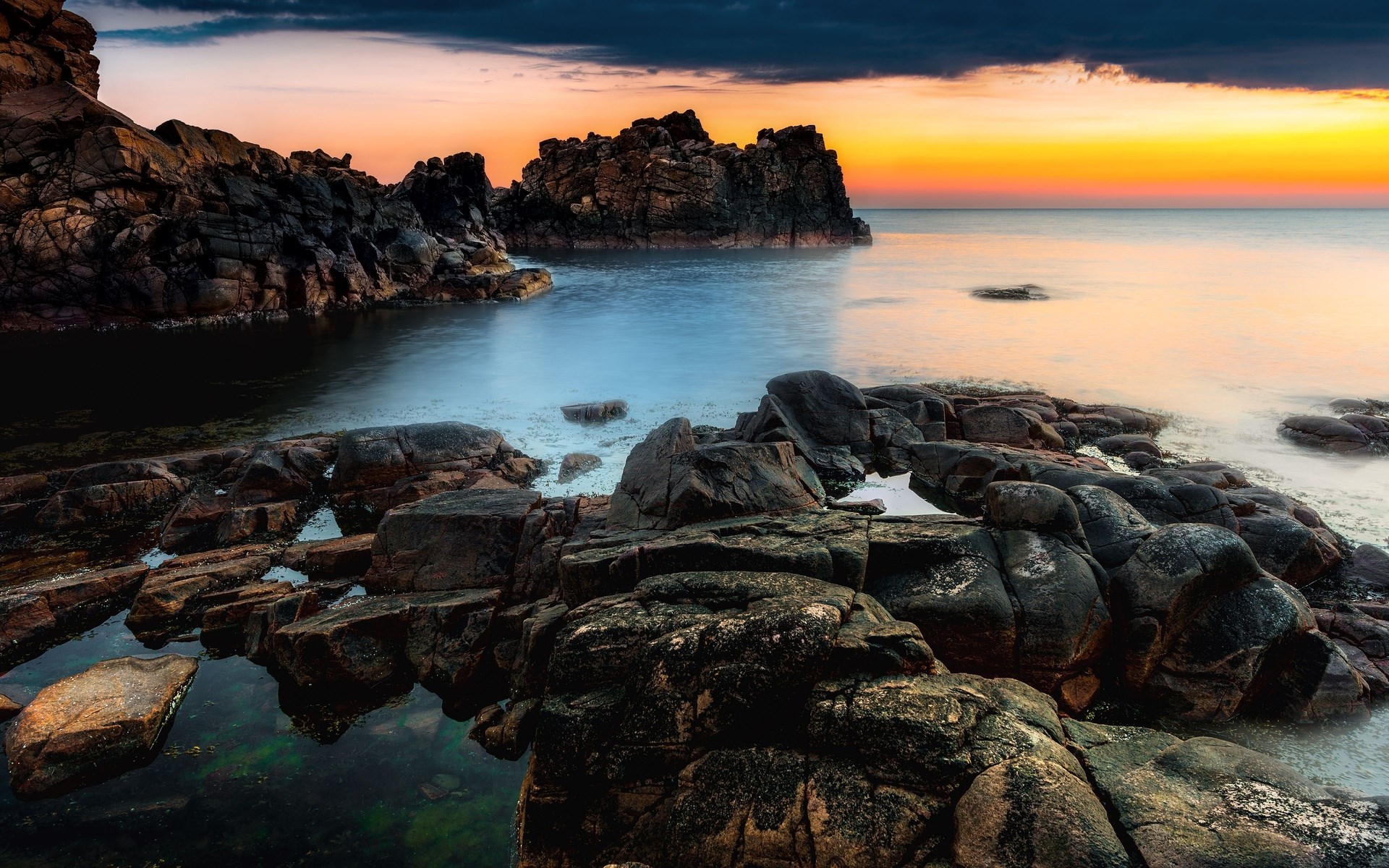 Rocky coastline at sunset with calm ocean HD Wallpaper