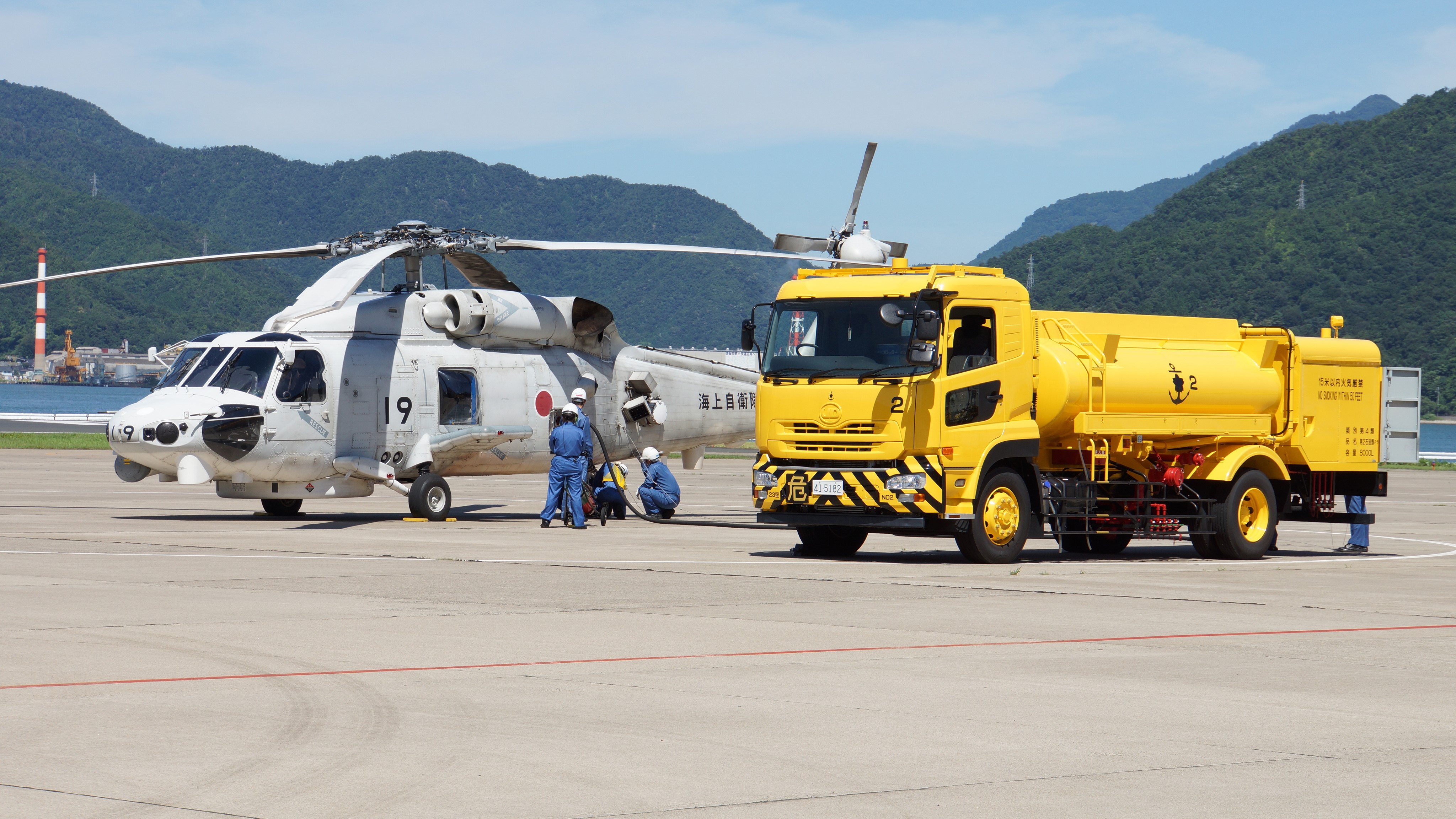Helicopter refueling by yellow tanker truck at airport HD Wallpaper