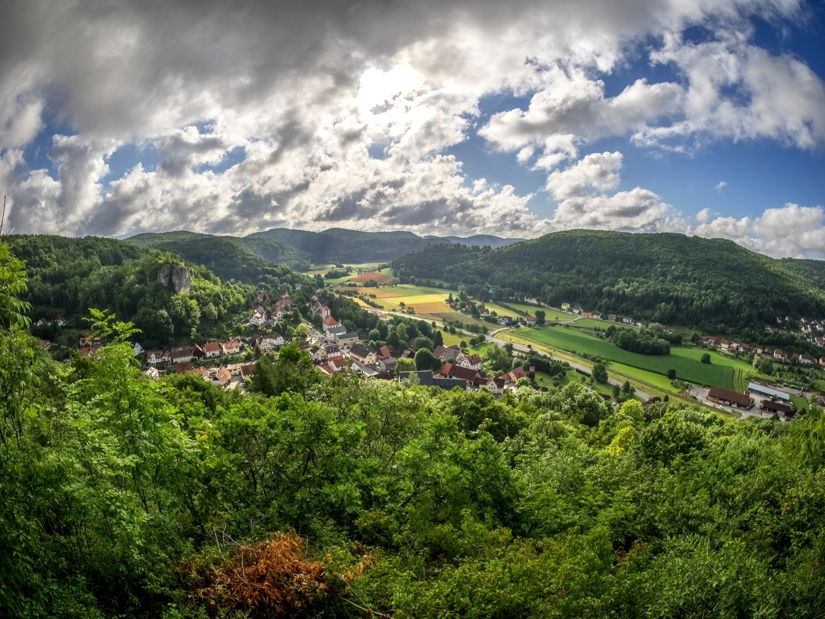 Village nestled in a green valley under a cloudy sky HD Wallpaper