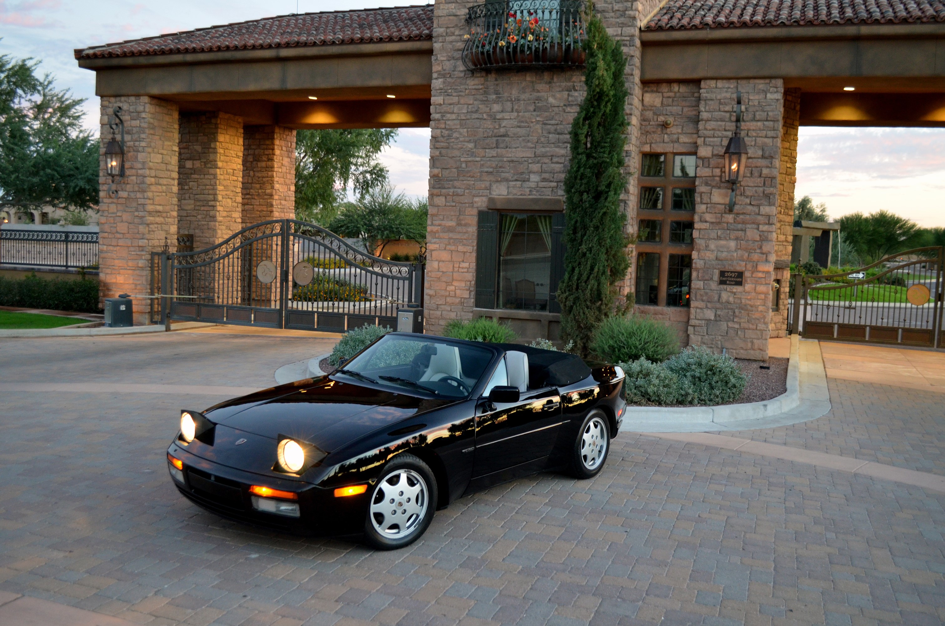 Black Porsche 944 S2 Cabriolet in front of a stone gatehouse HD Wallpaper