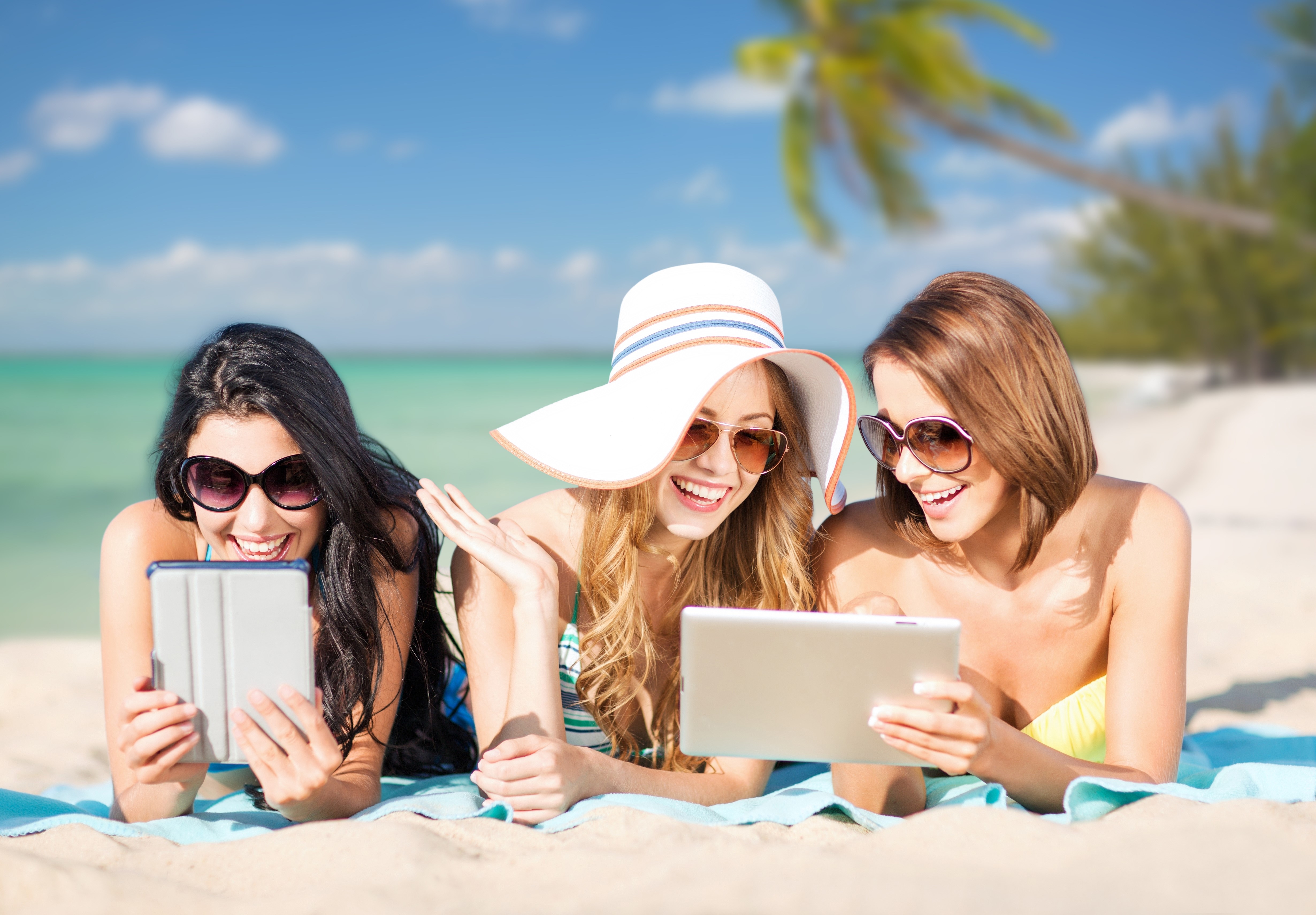 Three women with tablets on a beach HD Wallpaper