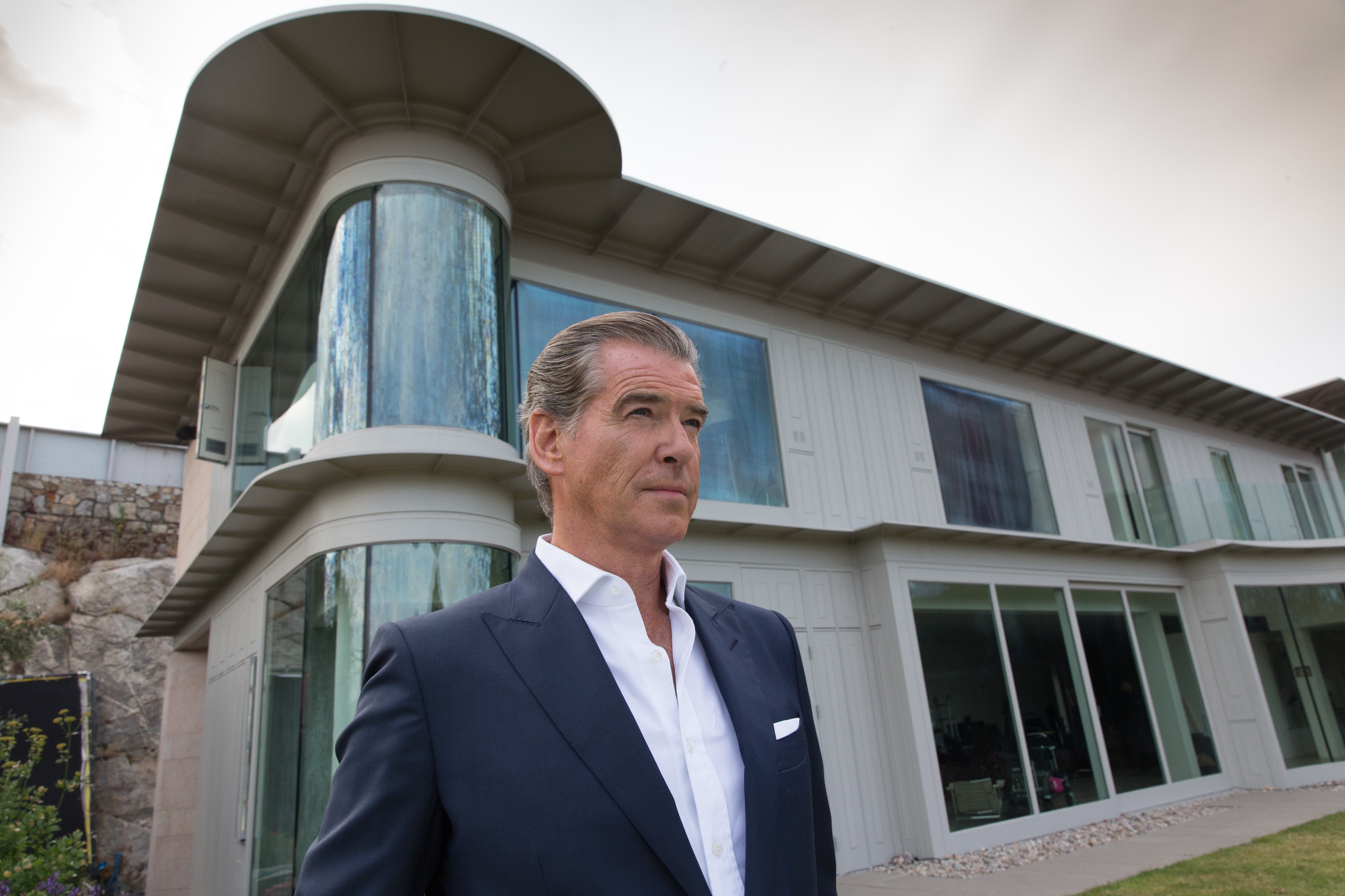 Pierce Brosnan in a suit in front of a modern house HD Wallpaper