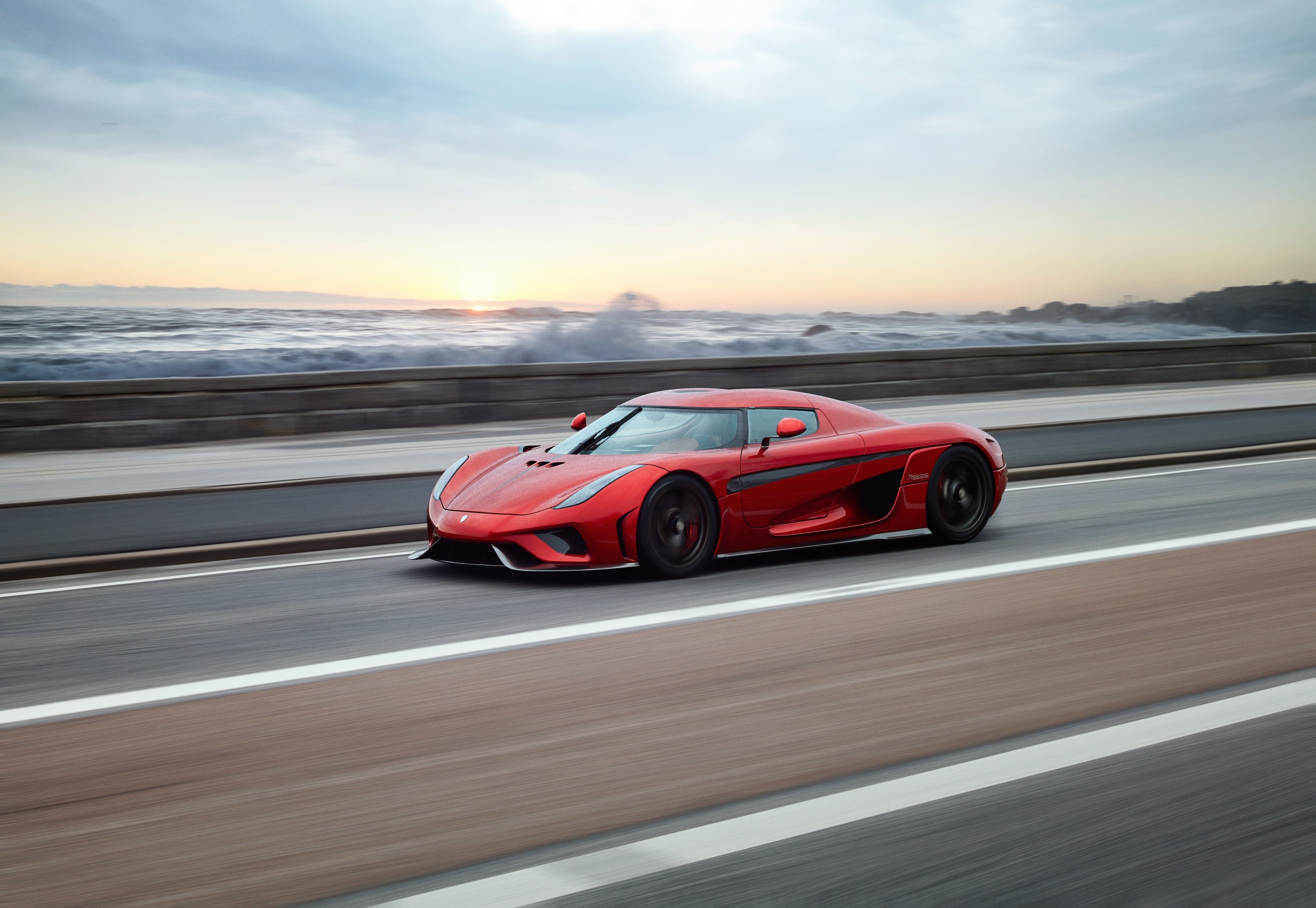 Red Koenigsegg Regera driving on a road by the ocean HD Wallpaper