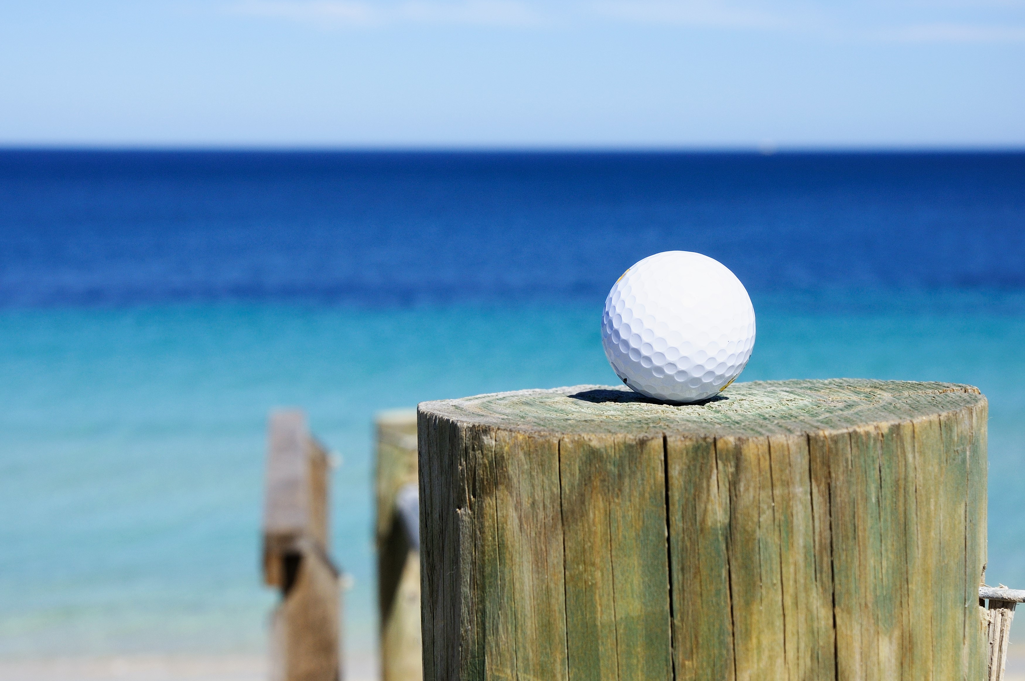 Golf ball on a wooden post by the ocean HD Wallpaper