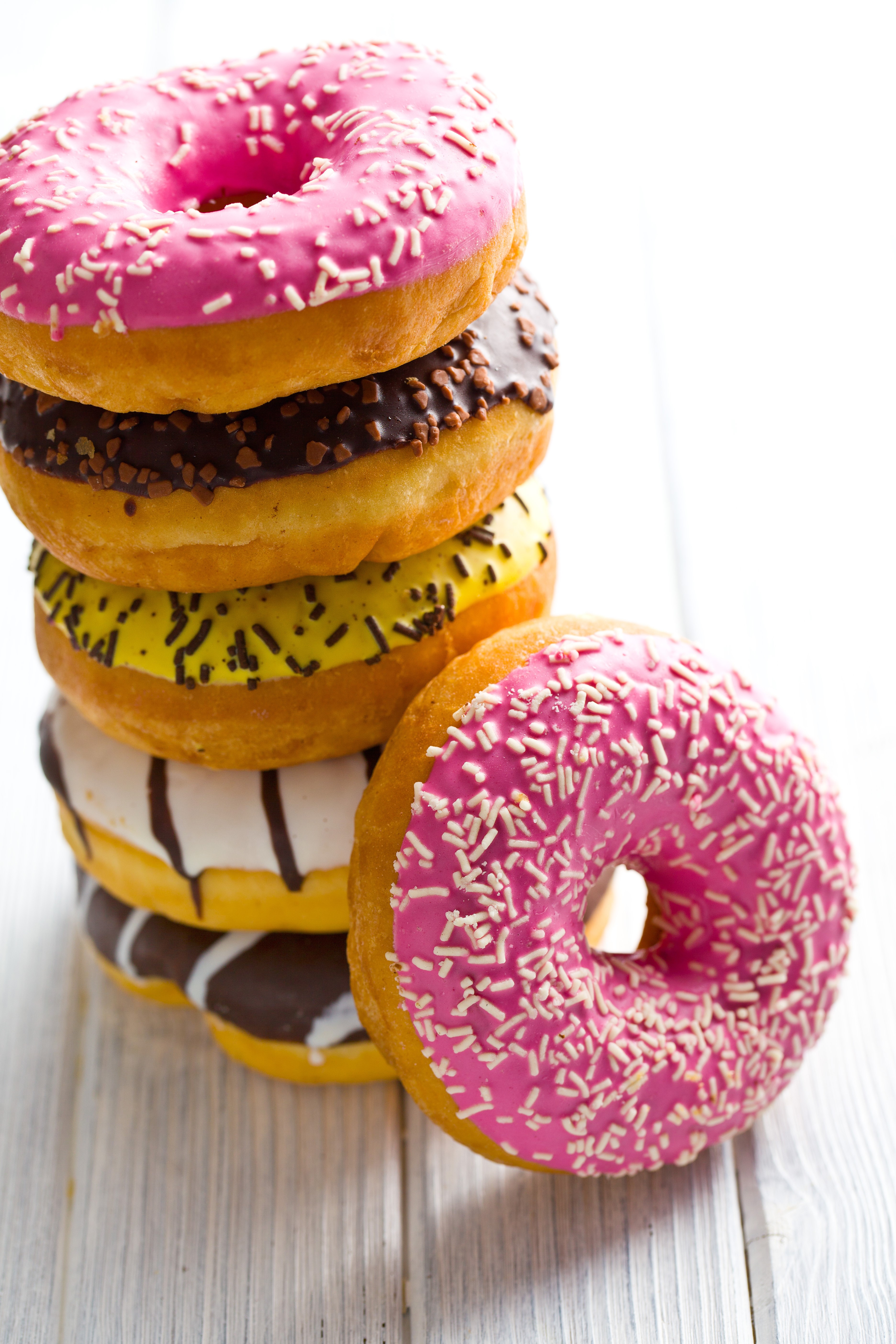 Stack of colorful donuts with sprinkles on wooden planks HD Phone Wallpaper