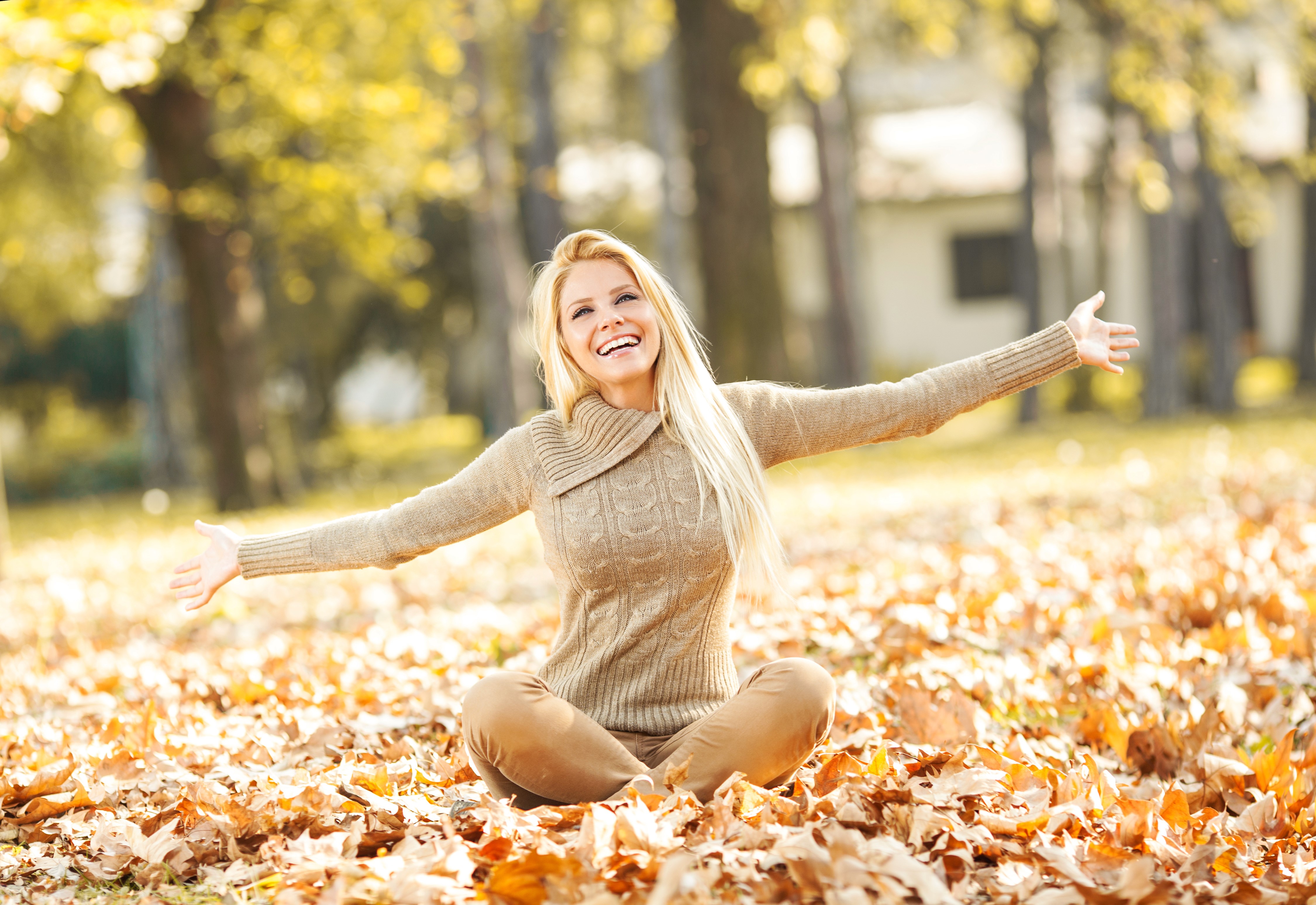 Blonde woman sitting in autumn foliage wearing a sweater HD Wallpaper