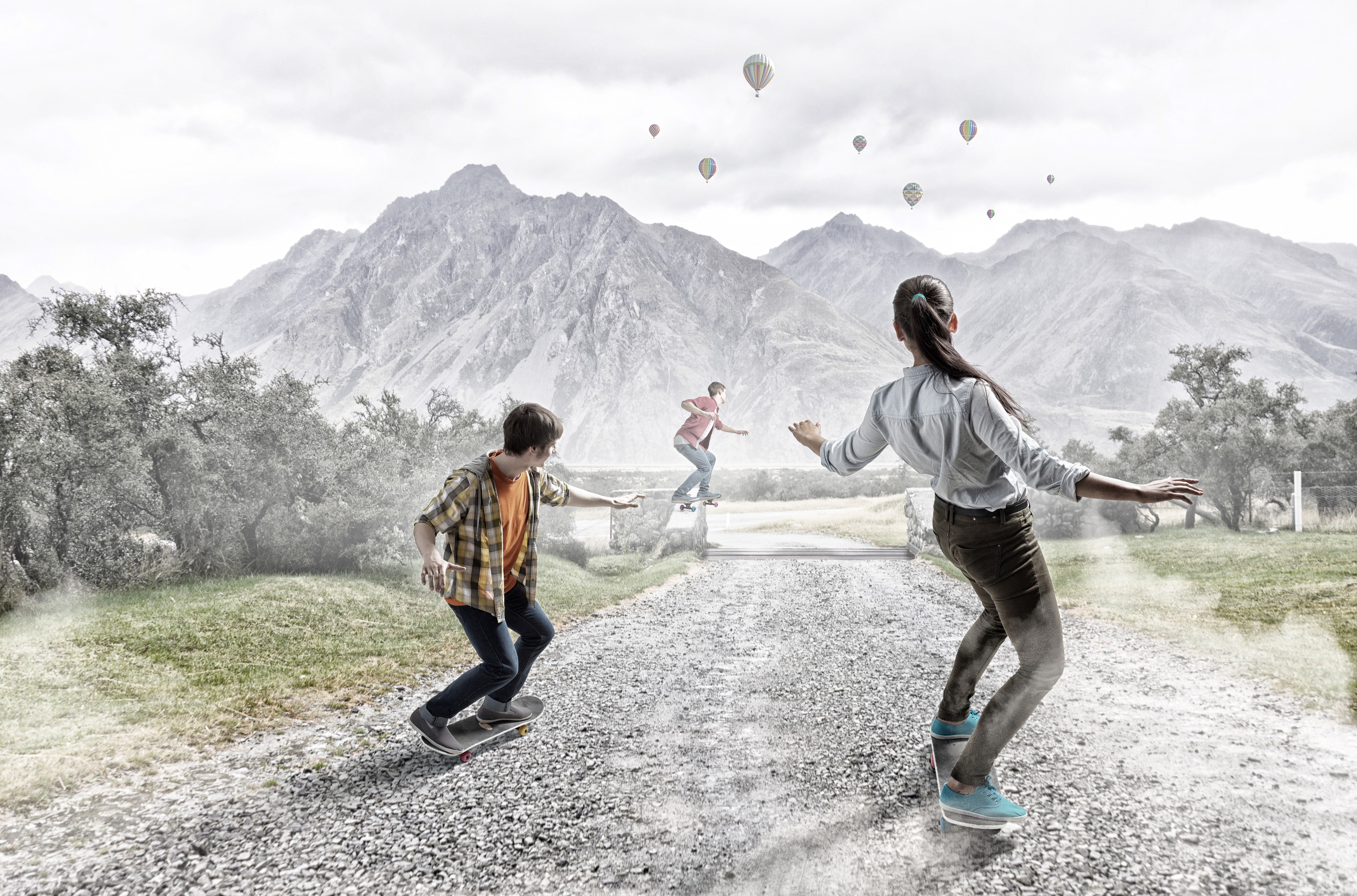 Three people skateboarding with mountains and hot air balloons HD Wallpaper