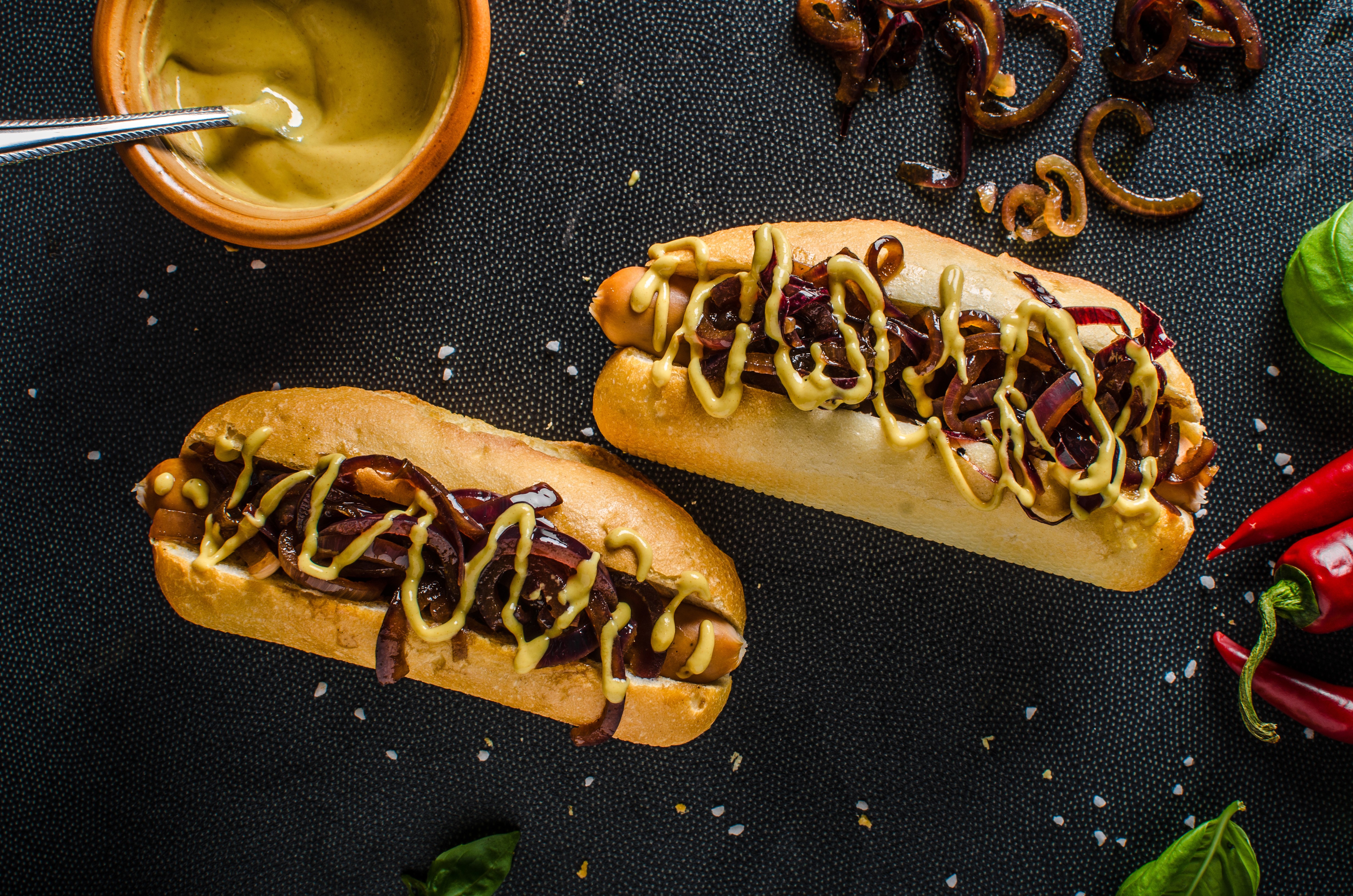 Two hot dogs with mustard and caramelized onions HD Wallpaper