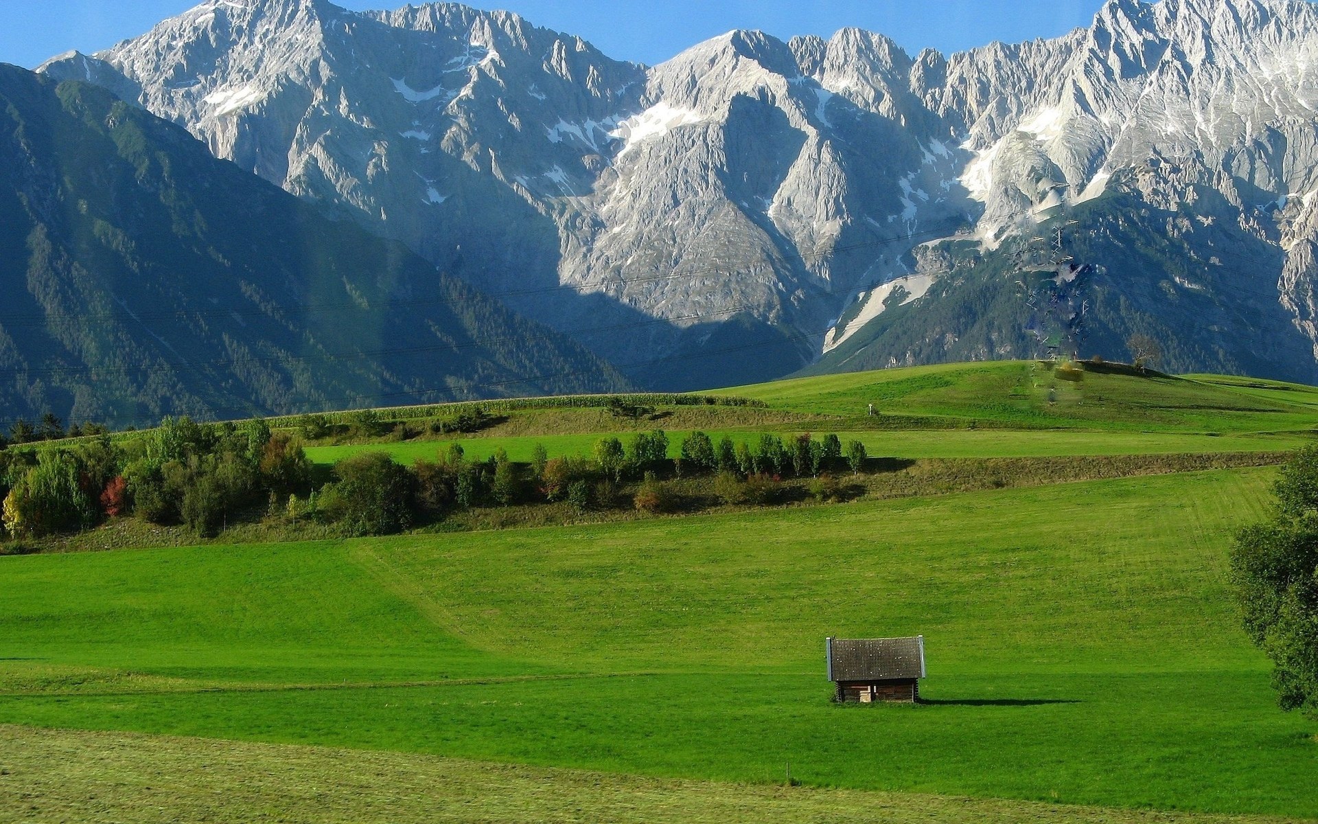 Small wooden cabin in a green meadow with mountains HD Wallpaper