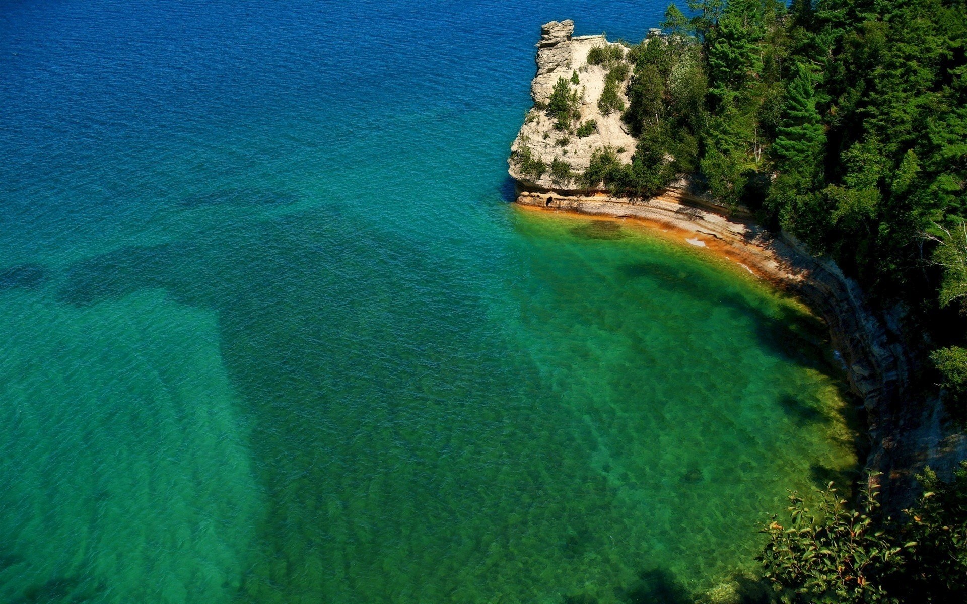 Rocky cliff face jutting into clear turquoise water HD Wallpaper