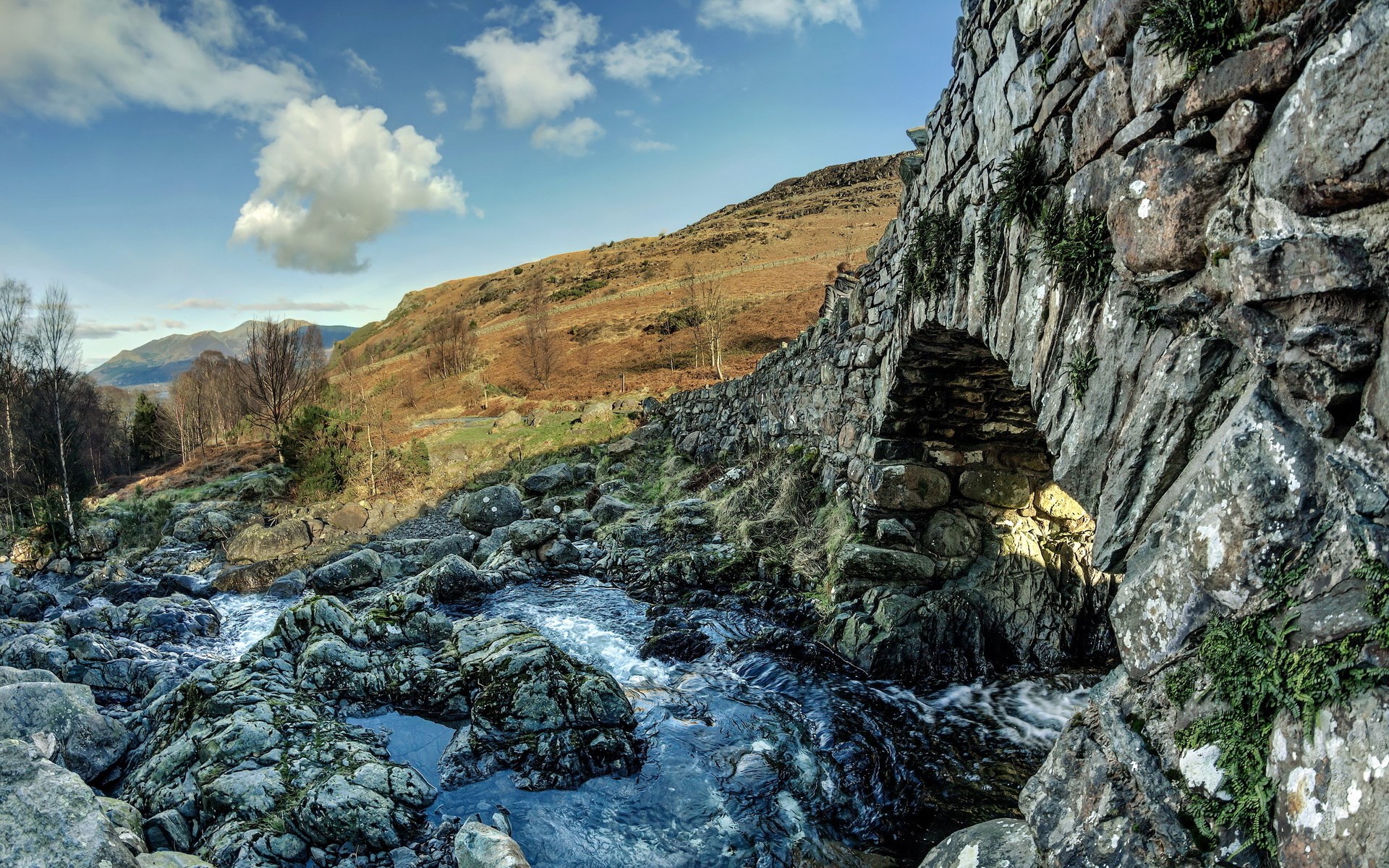 Stone bridge over a rocky stream with hills in background HD Wallpaper